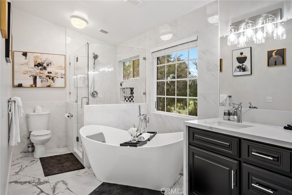 Bathroom with a freestanding tub, glass shower, dark vanity, and large window overlooking trees.