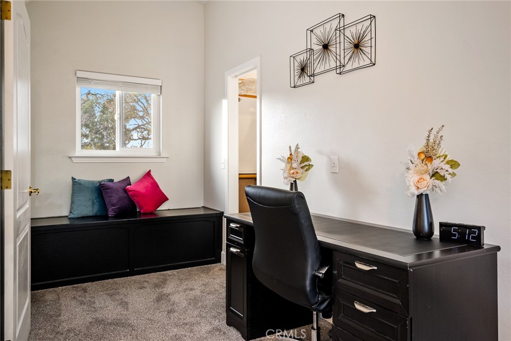 Furnished home office with a black desk, swivel chair, and window-seat bench.