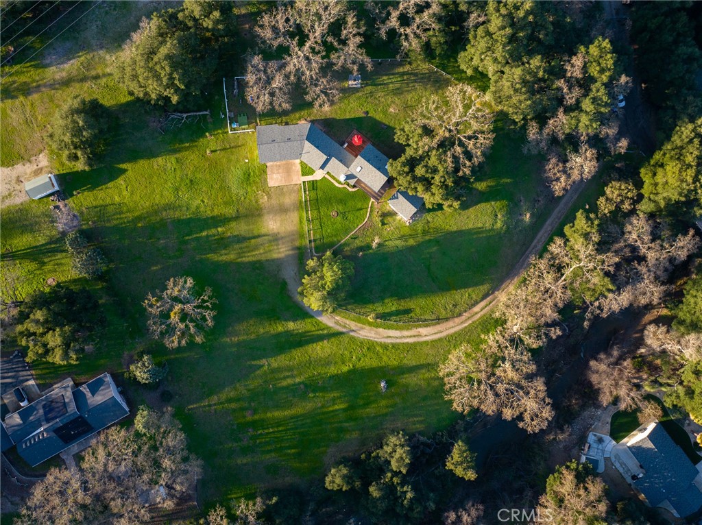 Aerial view of a home on a large green lot with mature trees and a curved driveway.