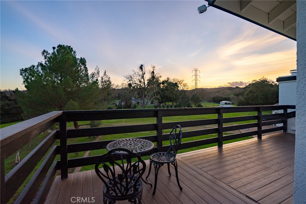 Wood deck with patio table overlooks a green, tree-lined rural landscape at sunset.
