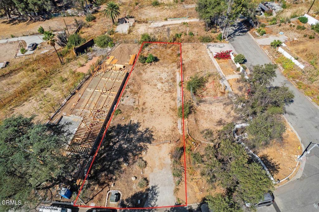 Aerial view of an undeveloped lot outlined in red beside a partially built structure.