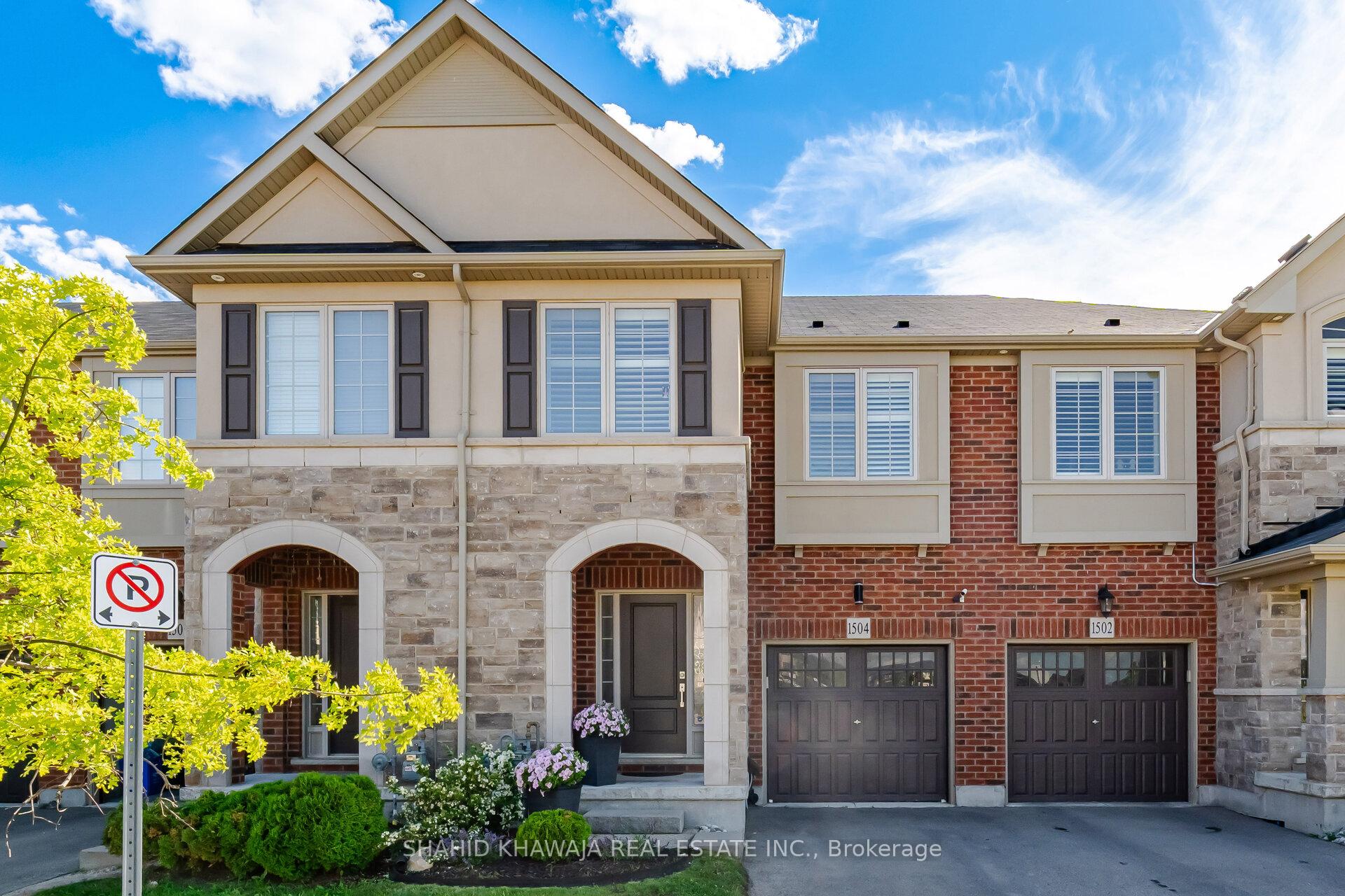 Two-storey brick and stone home with arched entryways, dark garage doors, and a small front garden.