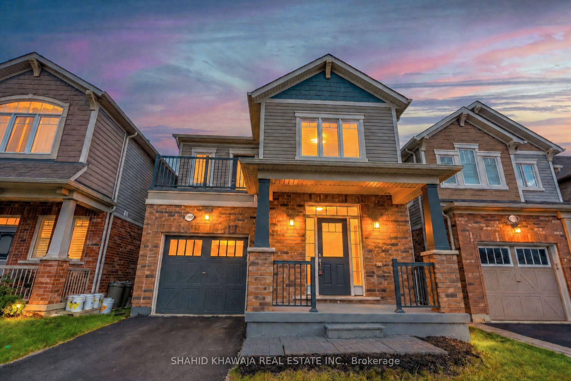 Two-story brick-front home with an attached garage, covered porch, and warmly lit windows at dusk.