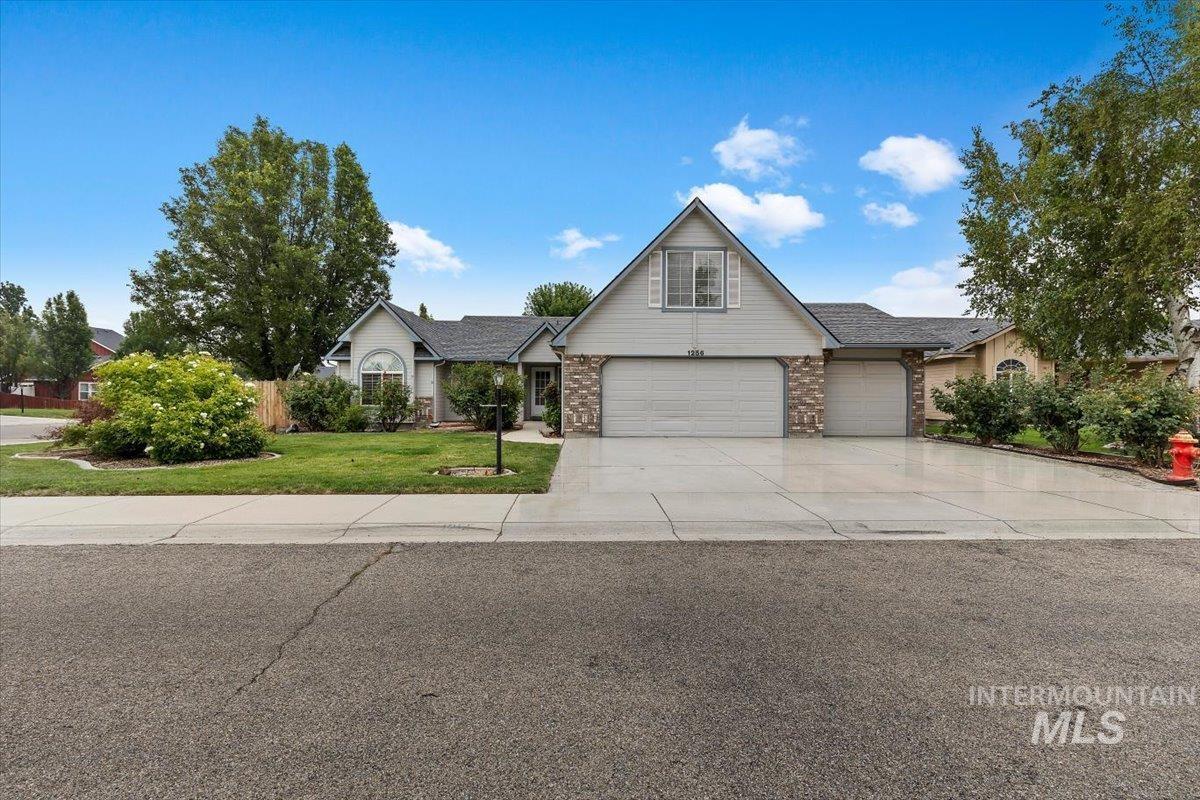 Suburban home with a peaked gable, three-car garage, stone accents, and landscaped front lawn.