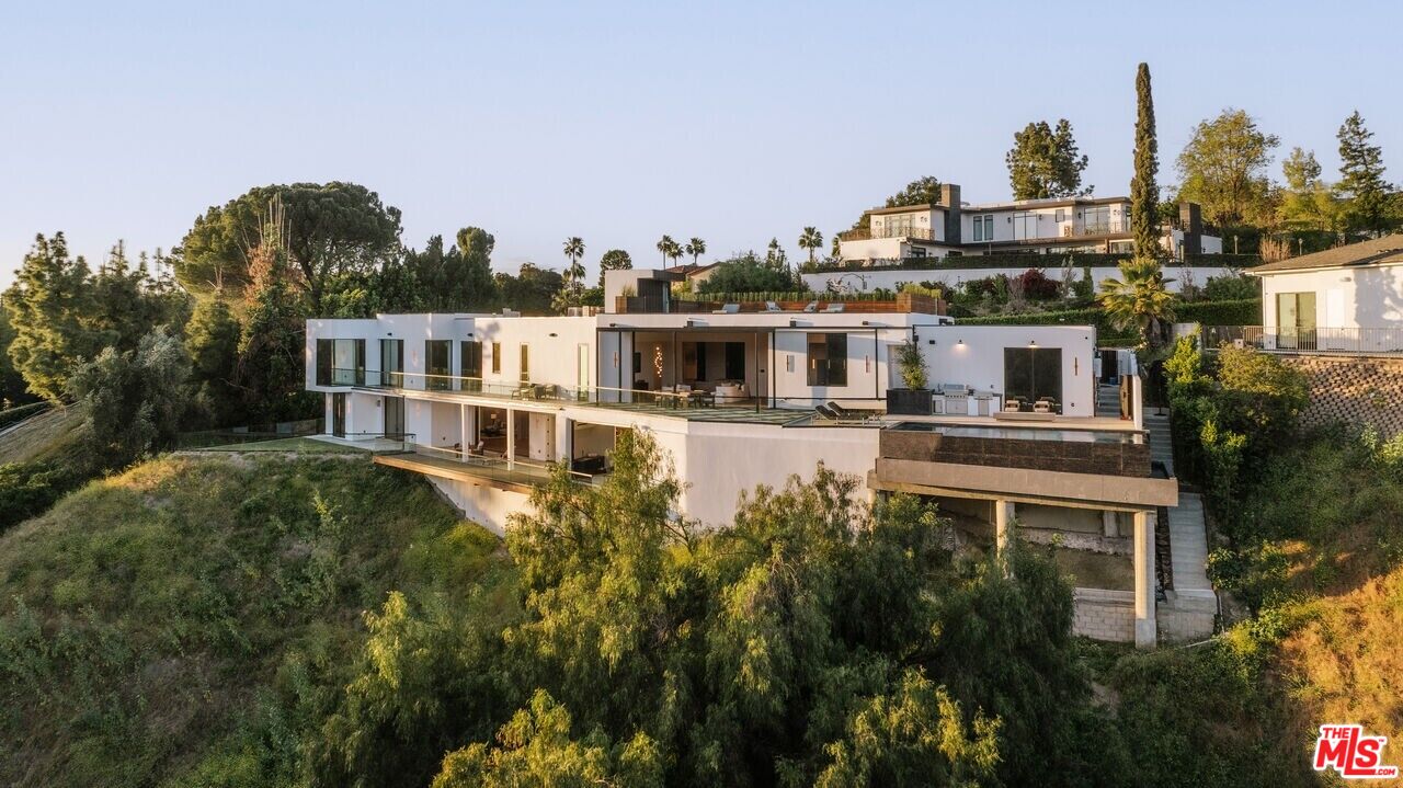 Contemporary hillside home with broad glass windows, multiple levels, and expansive terraces.