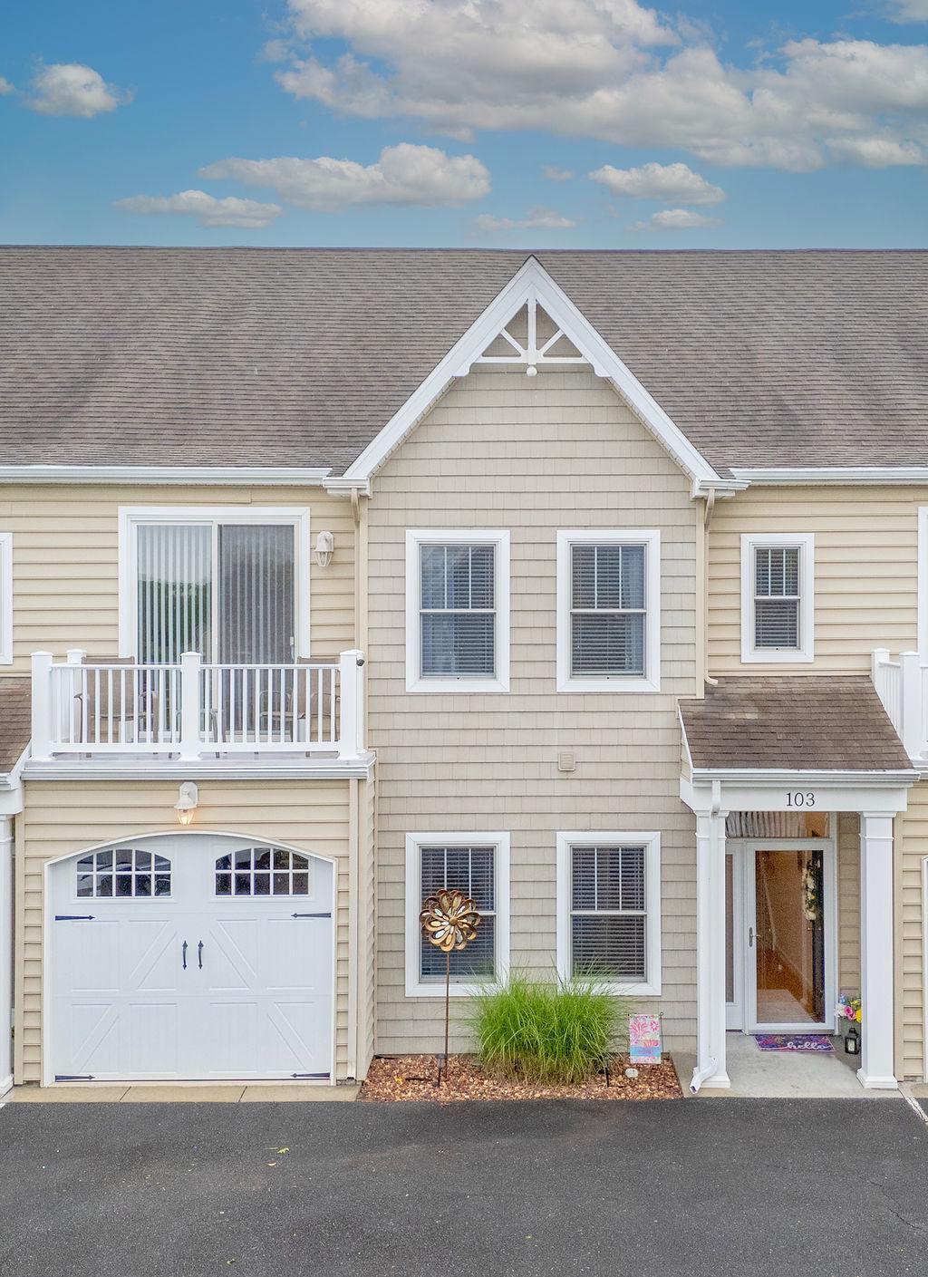Beige home exterior with a central gable, white garage door, and second-floor balcony.