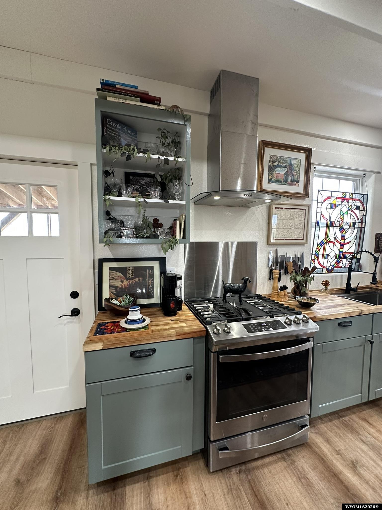 Kitchen with sage-green cabinets, butcher-block counters, stainless steel range, and a colorful stained-glass panel.