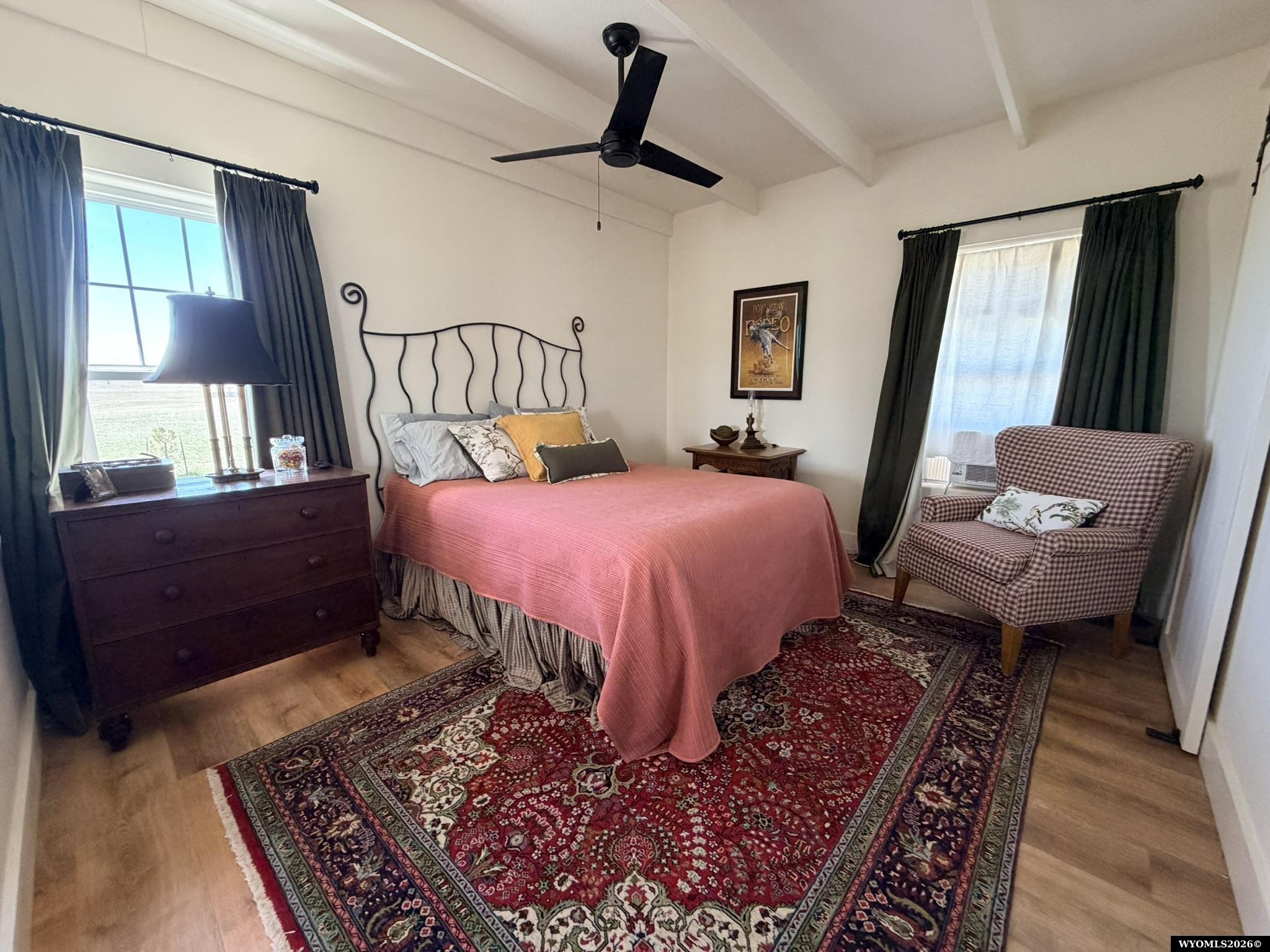 Bedroom with a coral-pink quilt, ornate metal headboard, patterned rug, and checked armchair.
