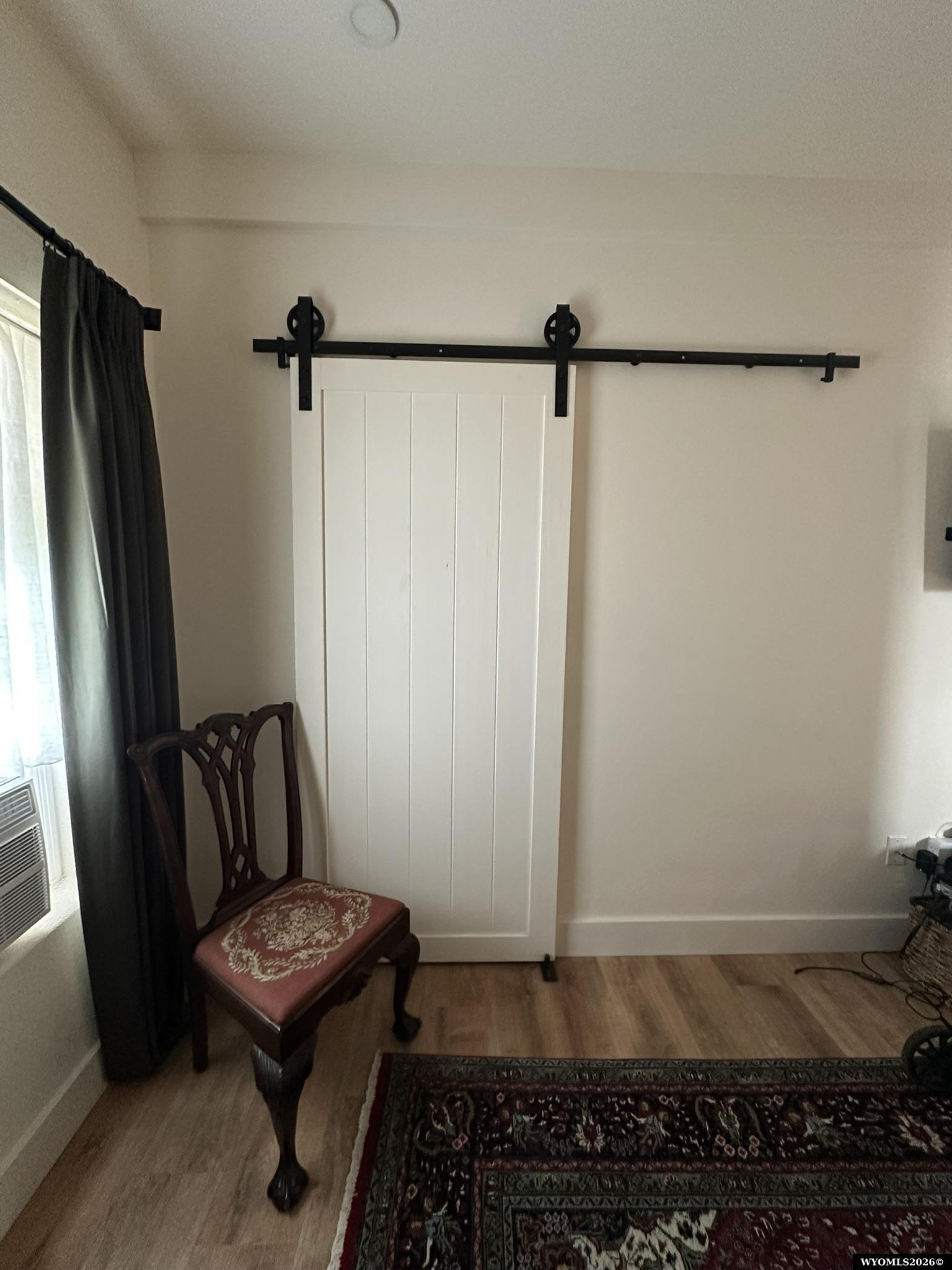 Room with a white sliding barn door, dark wood chair, curtained window, and patterned rug.
