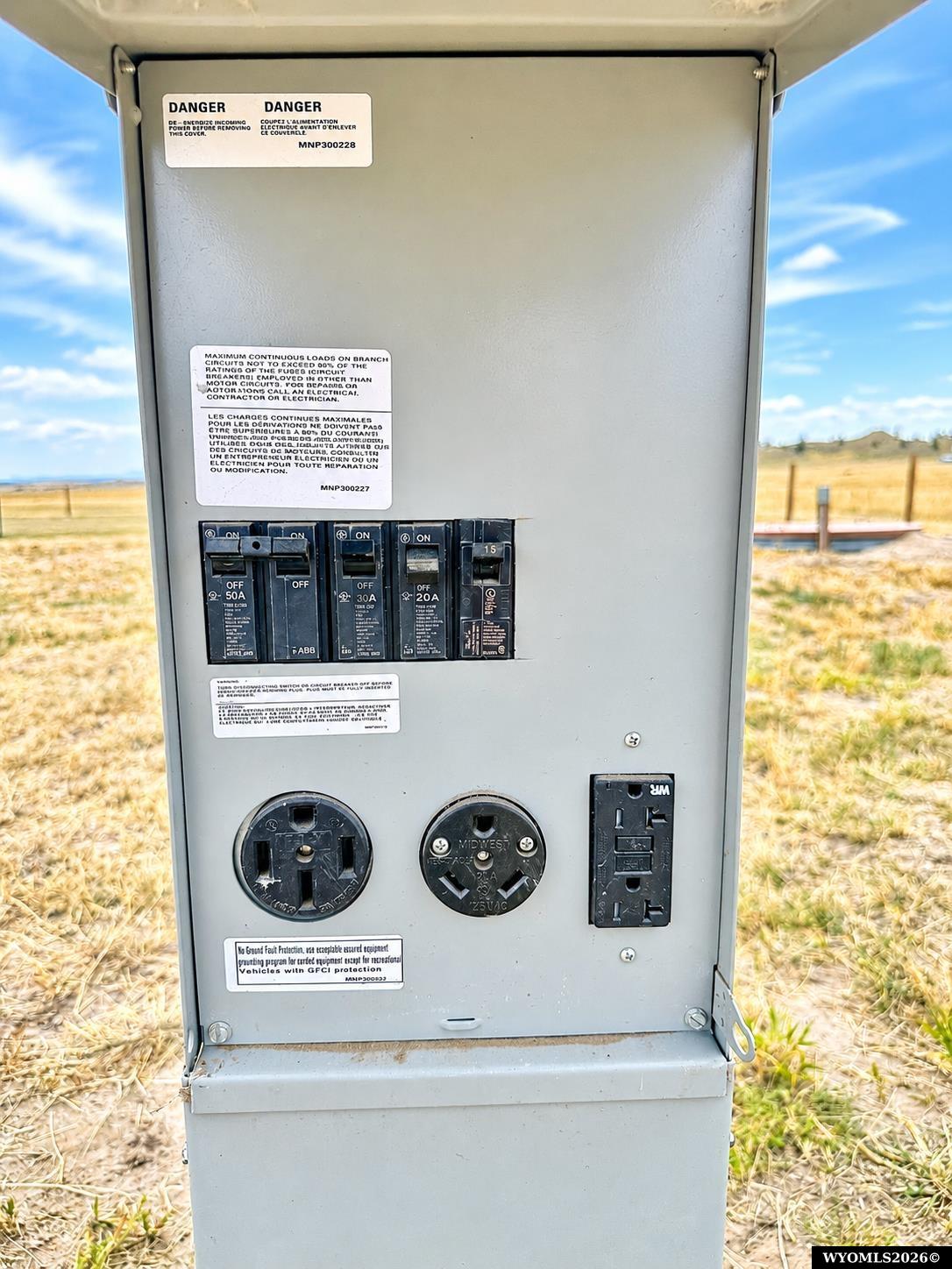 Outdoor electrical service panel with circuit breakers, round outlets, and a duplex receptacle.