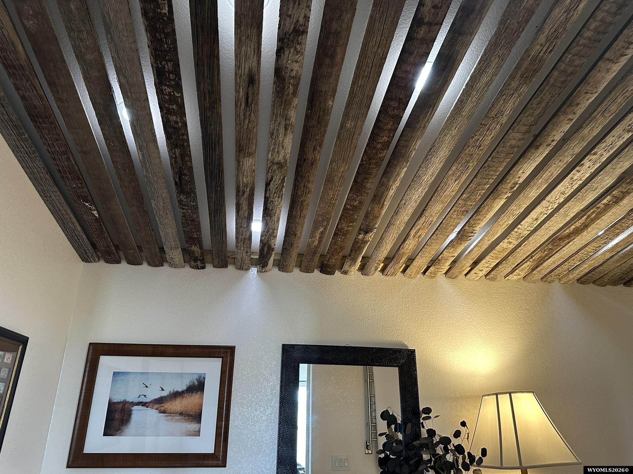 Interior ceiling with exposed rustic wooden beams above framed artwork and a mirror.