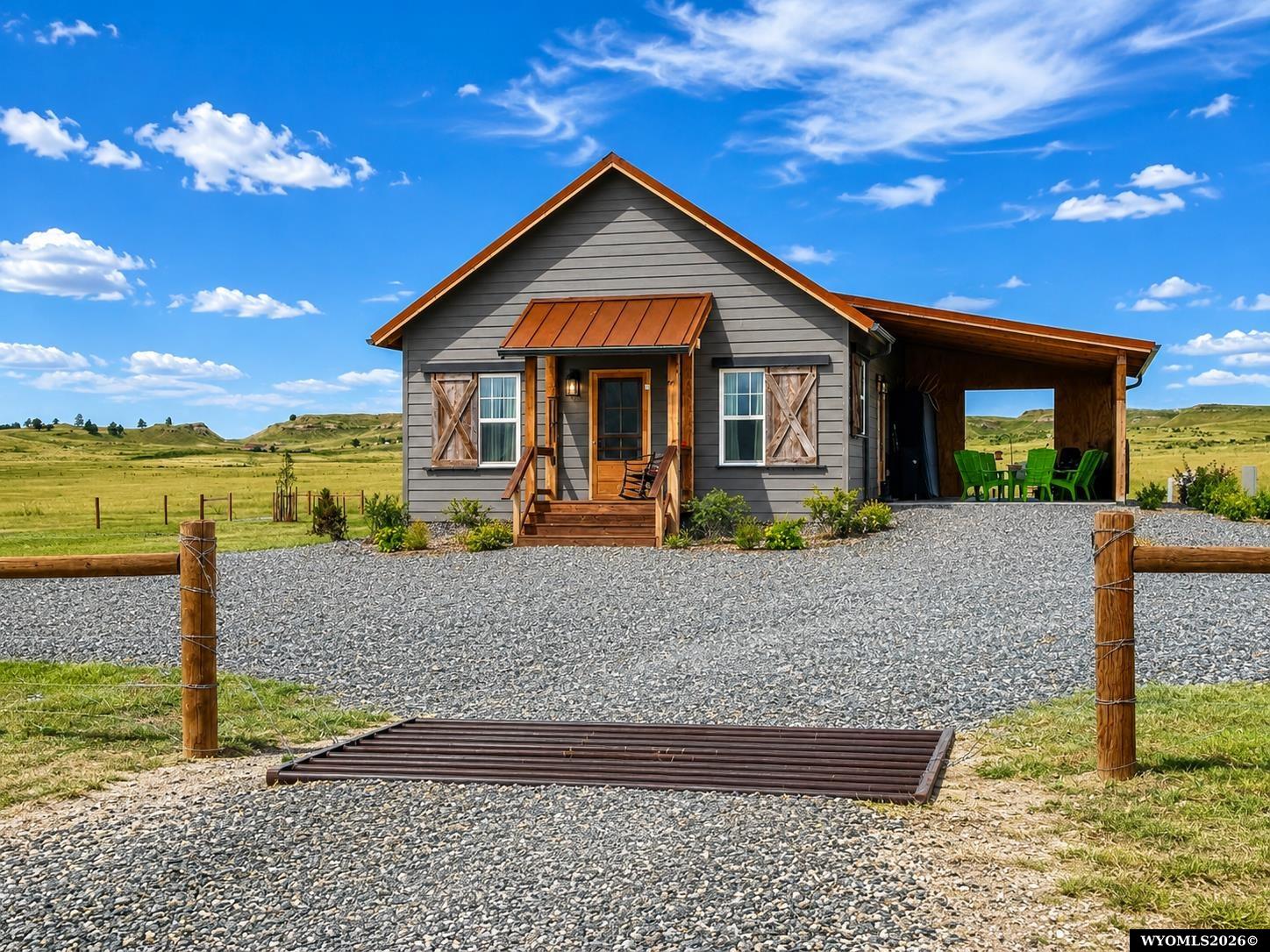 Gray gabled home with a wood-trimmed porch and covered patio amid open grassland.