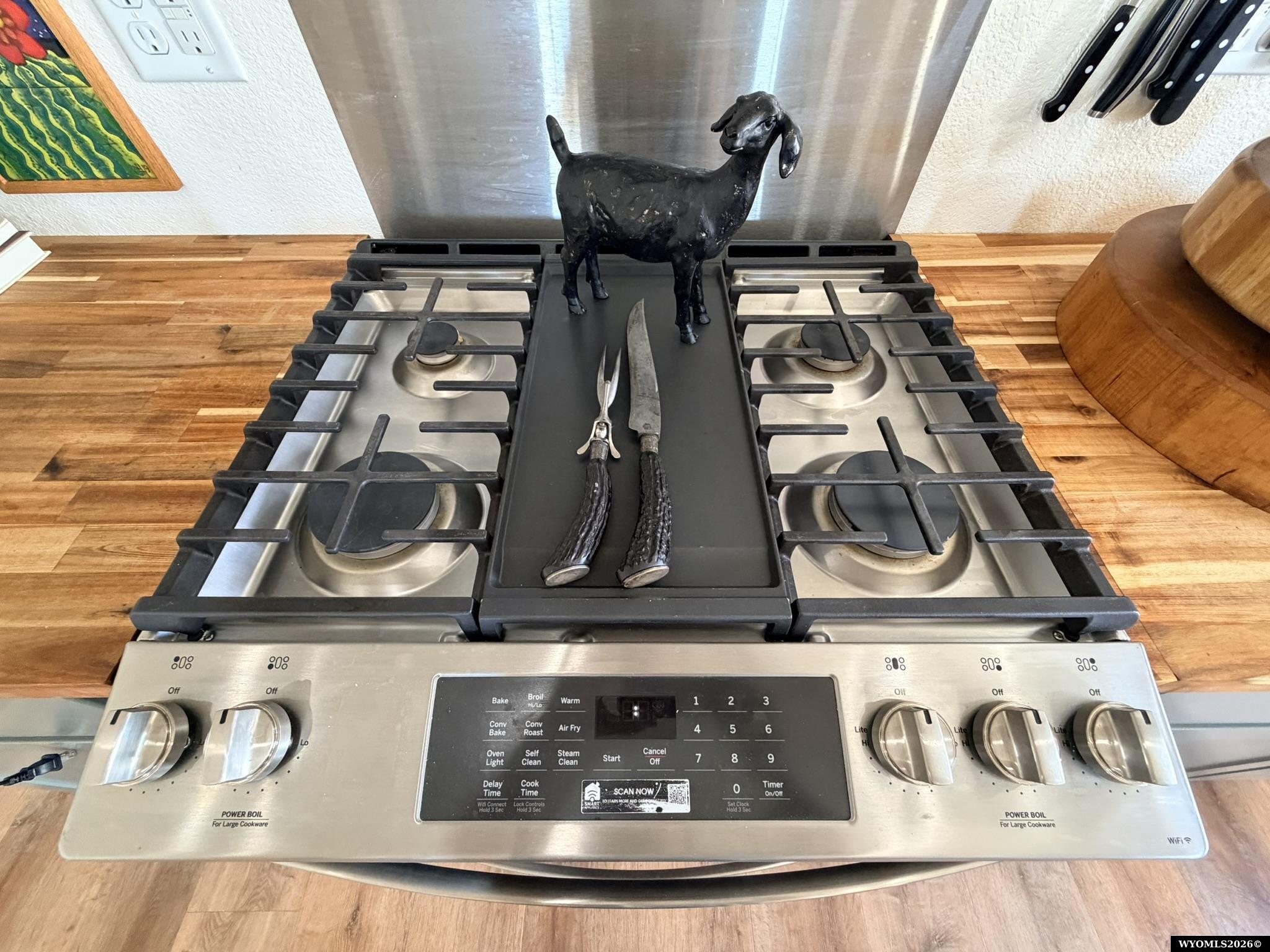 Kitchen gas range with a black goat figurine and decorative knives on the center griddle.