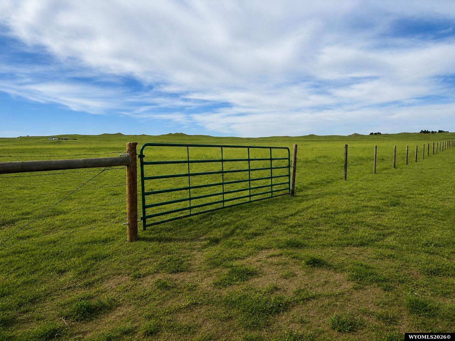 Fenced grassy acreage with a green metal gate and rolling hills.