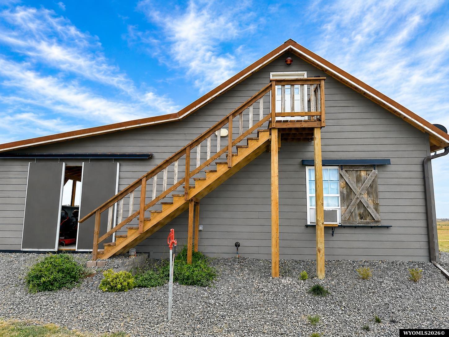Gray-sided property with a wooden exterior staircase leading to an upper balcony.