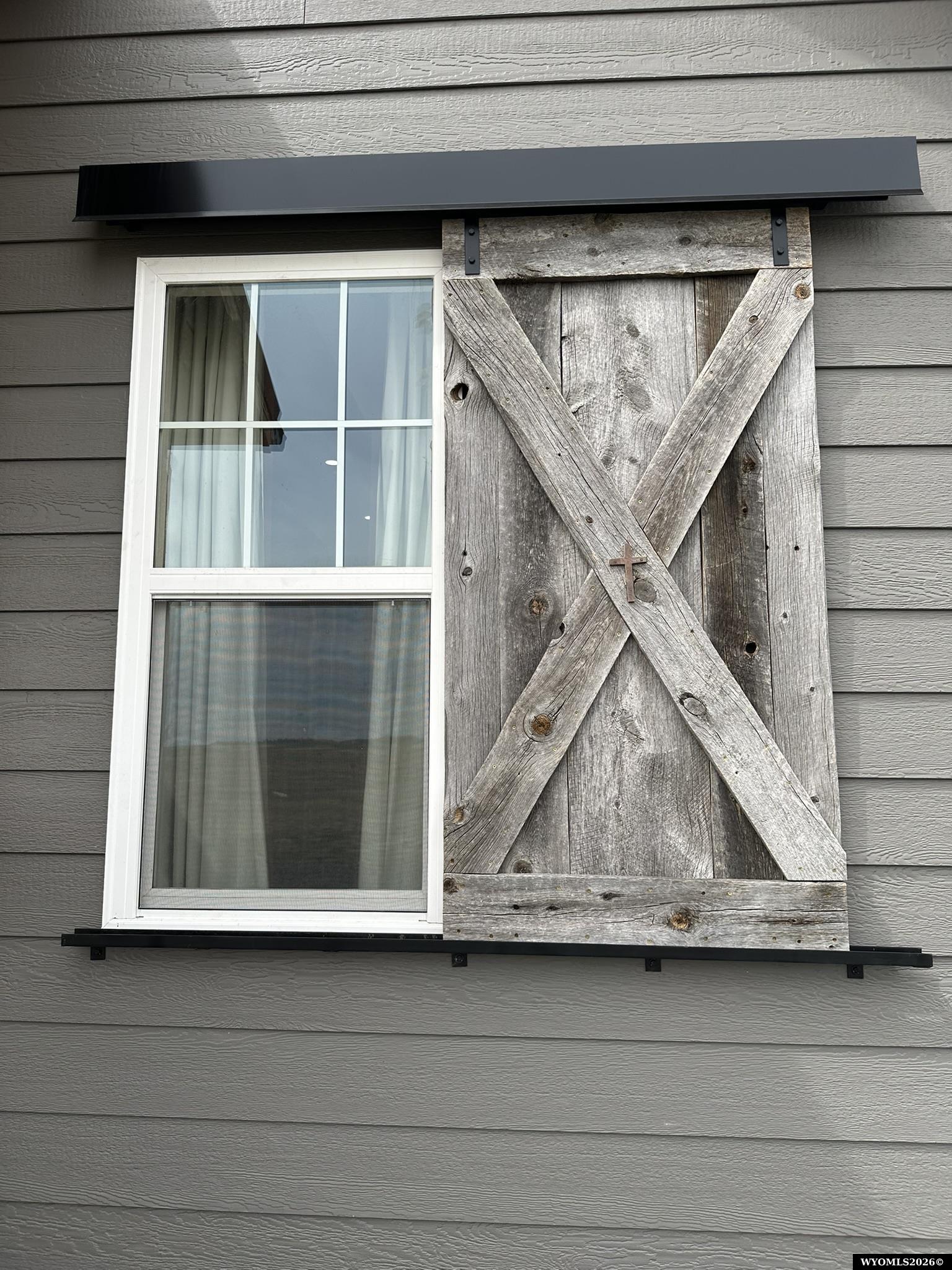 Exterior window beside a weathered wooden barn-style shutter with crossed boards.