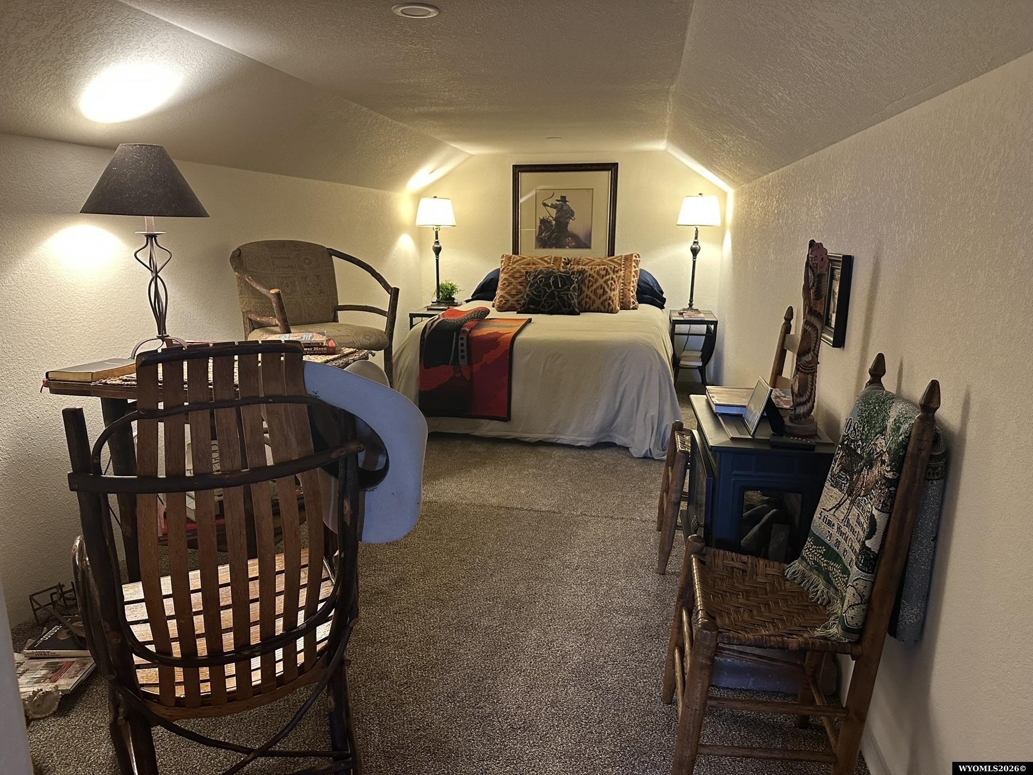 Furnished bedroom with a bed beneath a sloped ceiling and rustic wooden chairs.