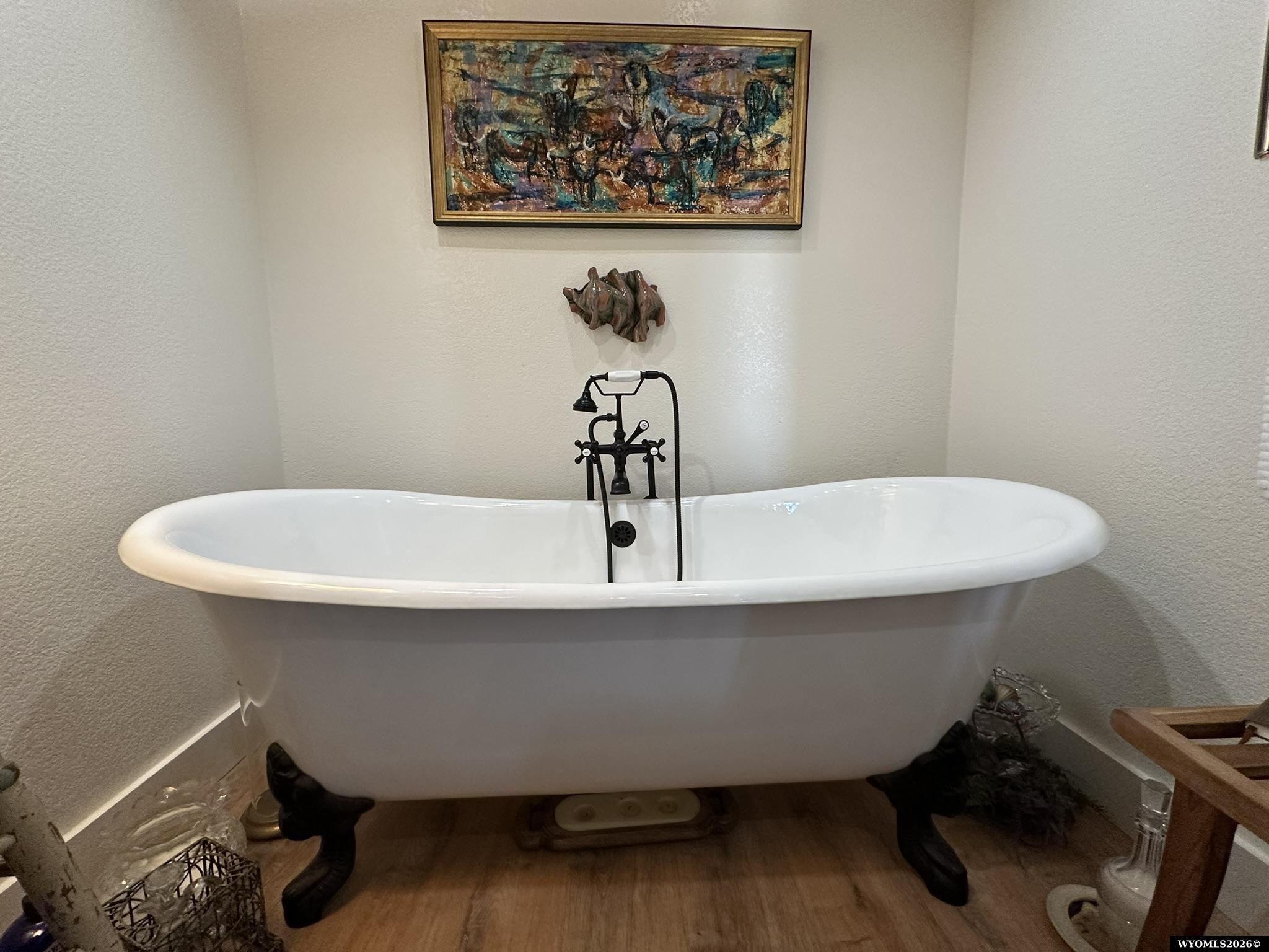 White clawfoot bathtub with black feet and vintage-style faucet beneath framed artwork.