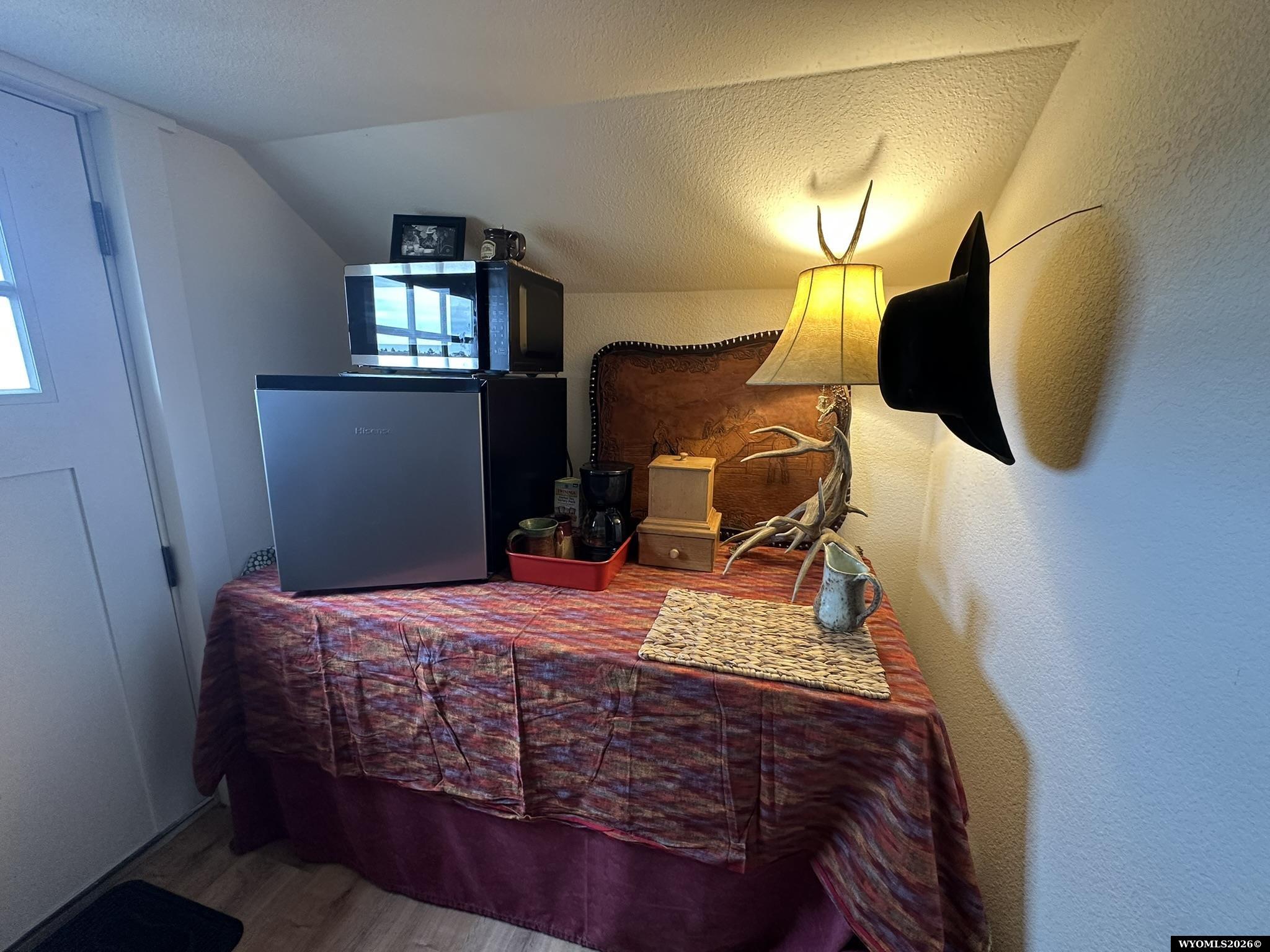 Compact kitchenette with a mini fridge, microwave, coffee maker, and western decor beneath a sloped ceiling.