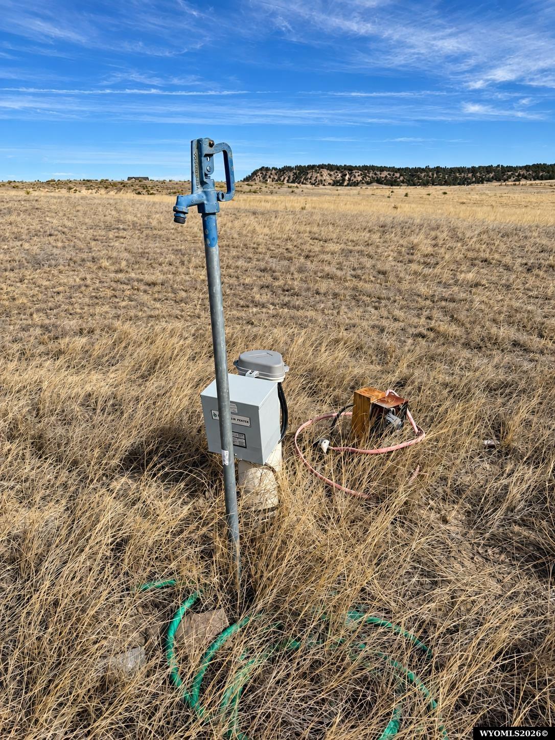 Vacant grassy lot with utility equipment and marked underground lines beneath a blue sky.
