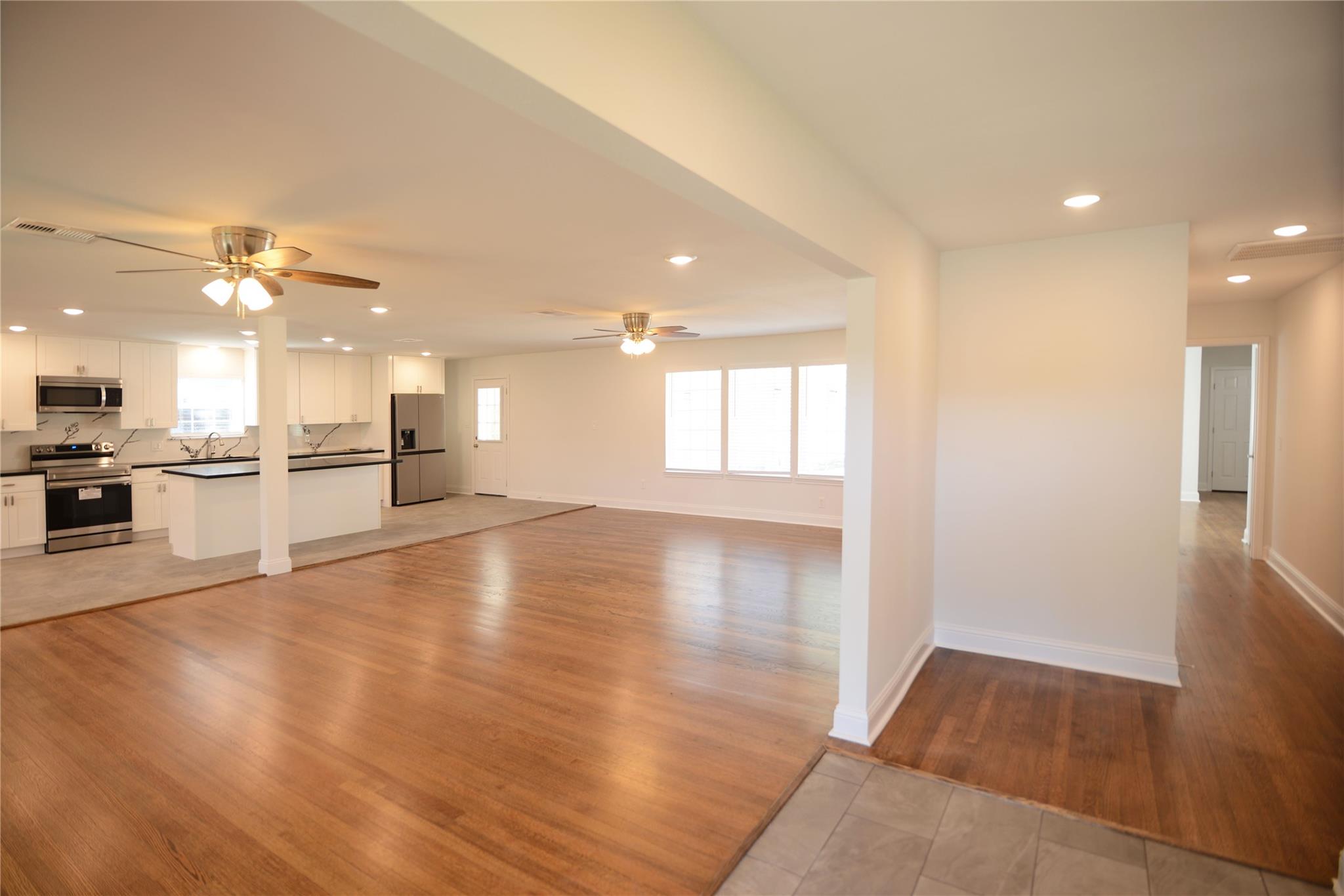 Open-plan living room and kitchen with hardwood floors, white cabinetry, and stainless steel appliances.