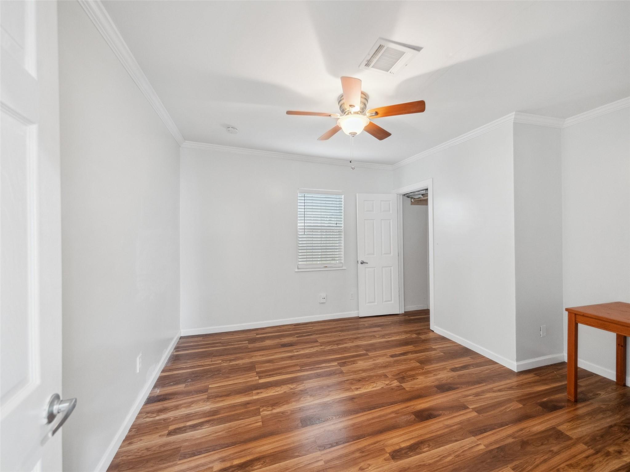 Empty bedroom with wood-look floors, a ceiling fan, and an open closet.