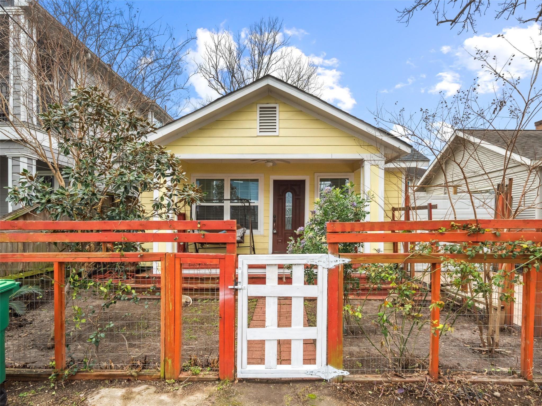 Yellow single-story house behind a red-orange fence and white gate.
