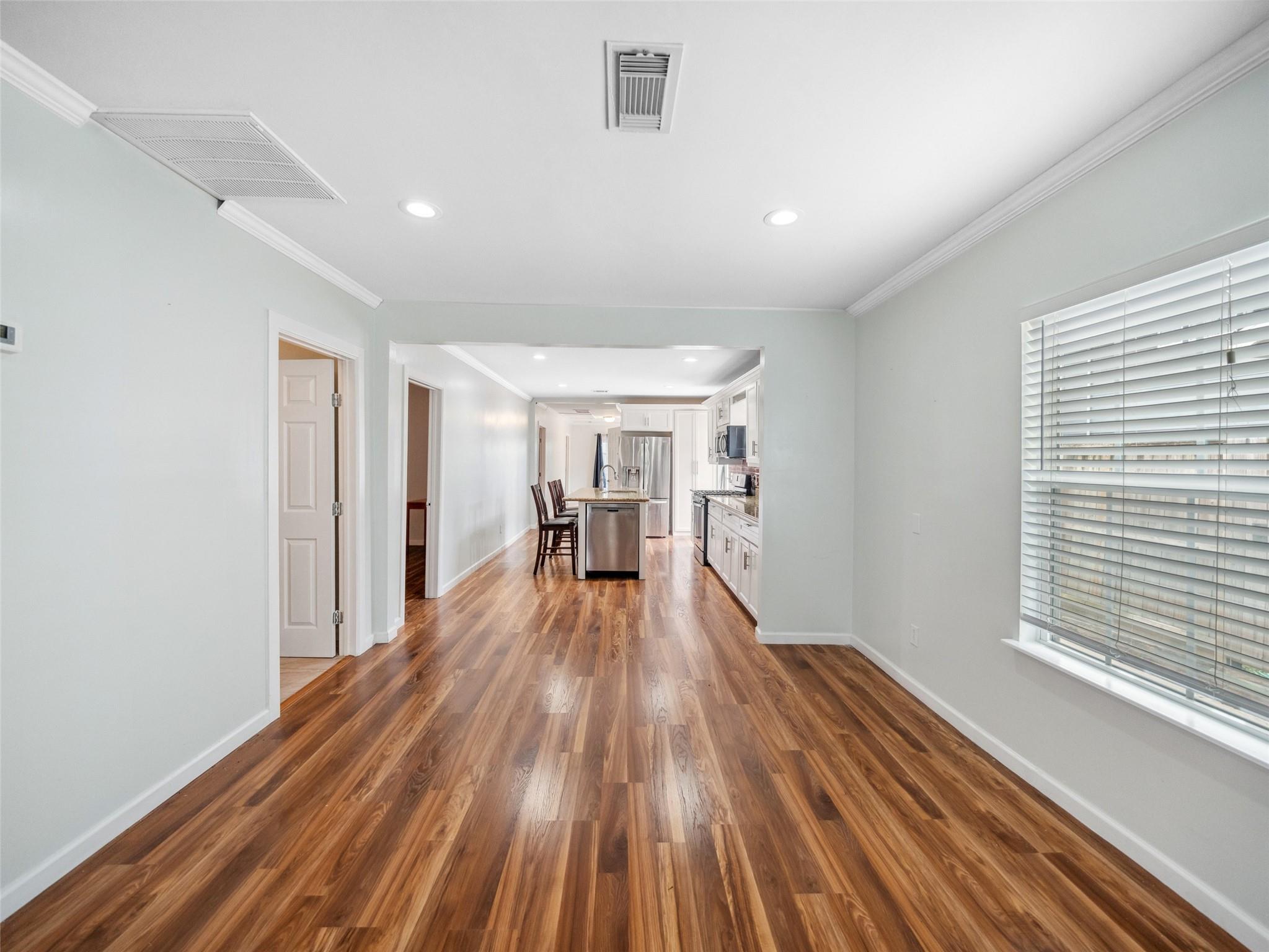 Open living area with glossy wood floors leading to a white kitchen and stainless steel island.