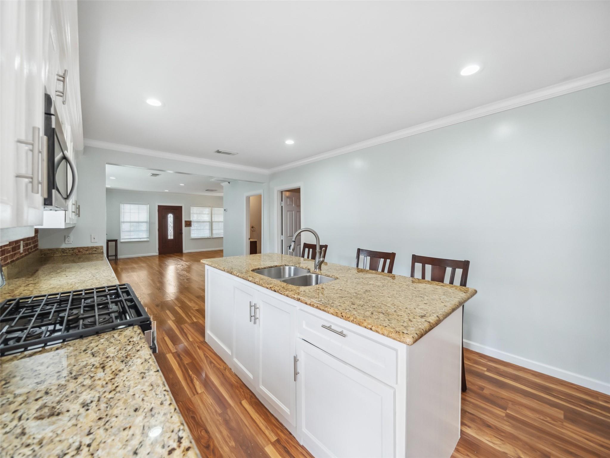 Open kitchen with a granite island, double sink, gas cooktop, and warm hardwood floors.
