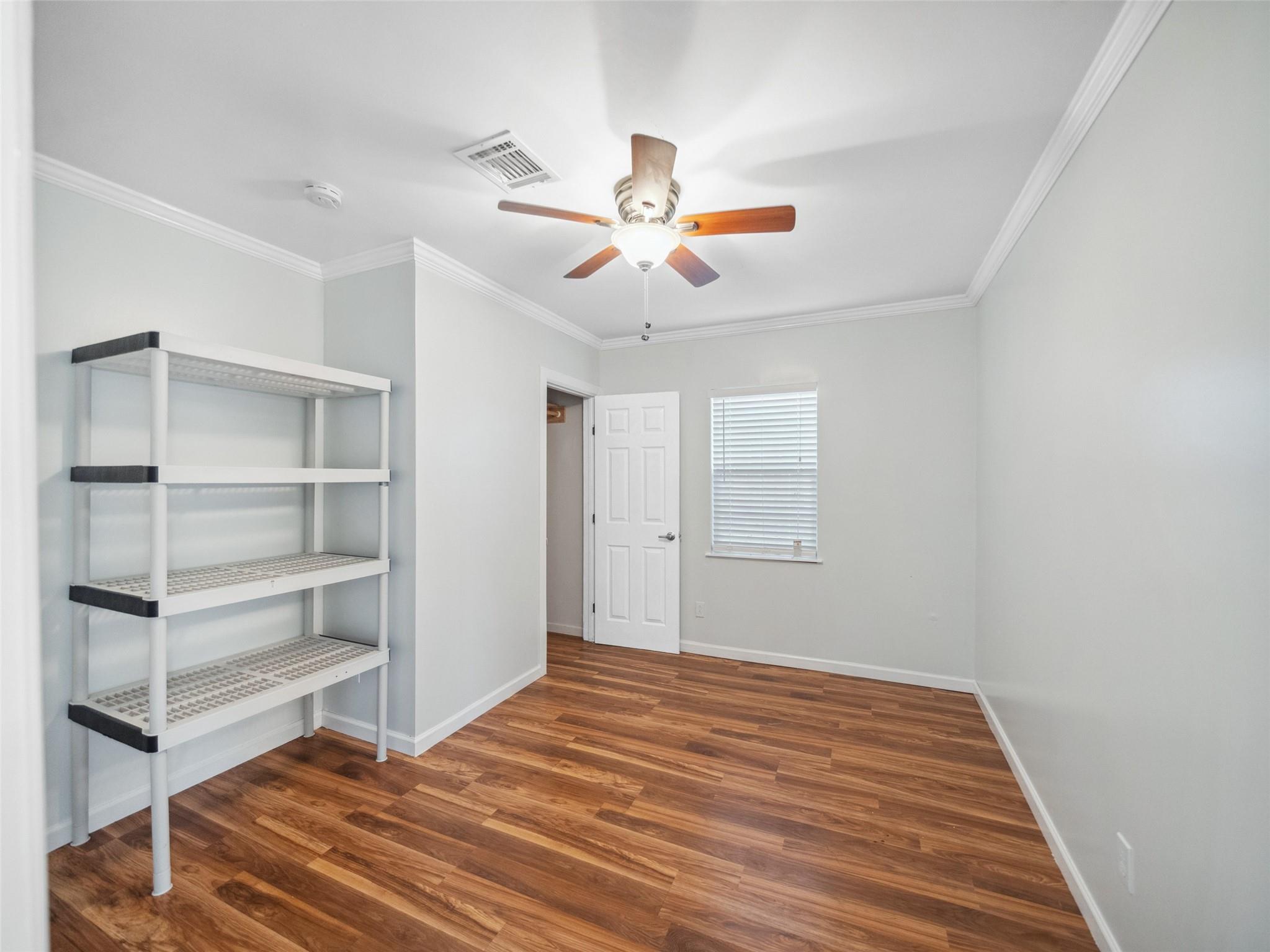 Empty room with wood-look flooring, open shelving, a ceiling fan, and a window with blinds.