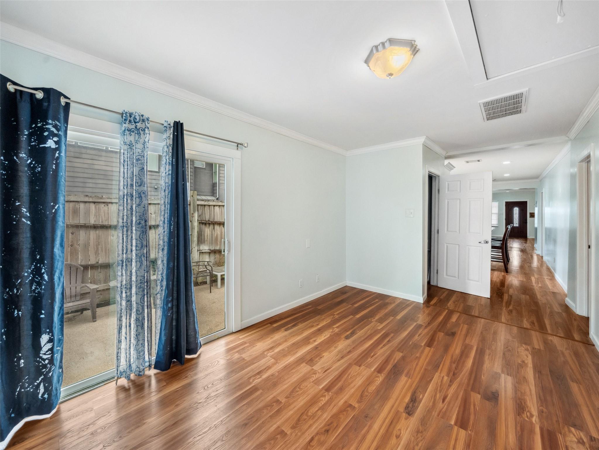 Empty room with wood floors and a curtained sliding glass door opening to a fenced patio.