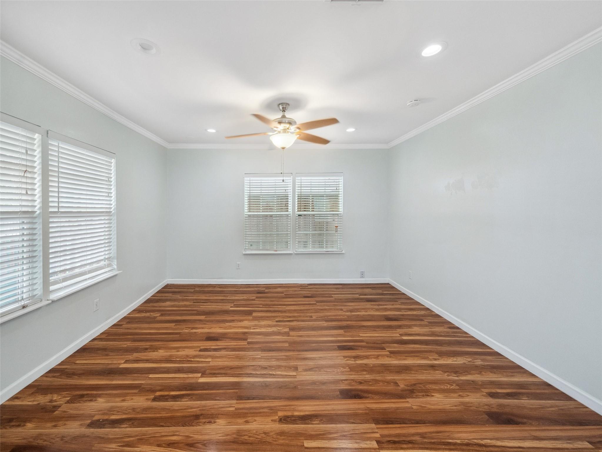 Vacant room with wood-look plank flooring, several blinded windows, and a ceiling fan with light.