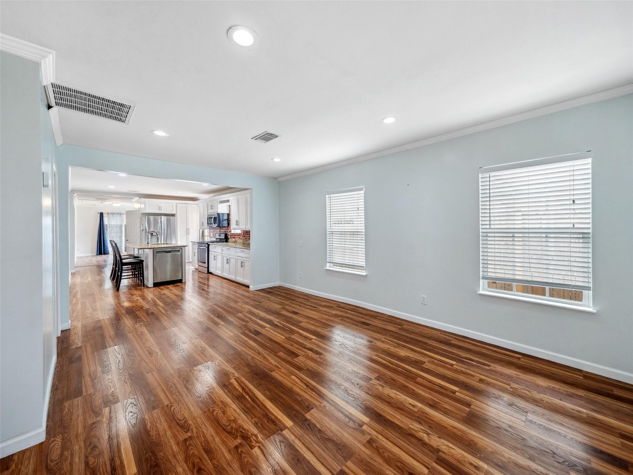 Open living area with glossy hardwood floors and a white kitchen beyond.