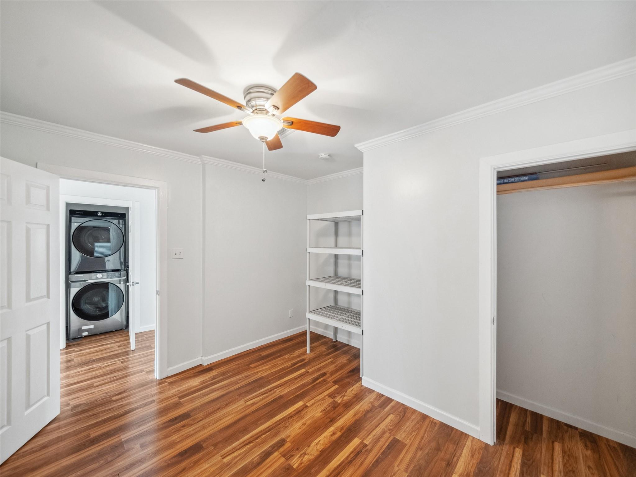 Laundry and storage area with wood floors, open shelving, and a stacked washer and dryer.