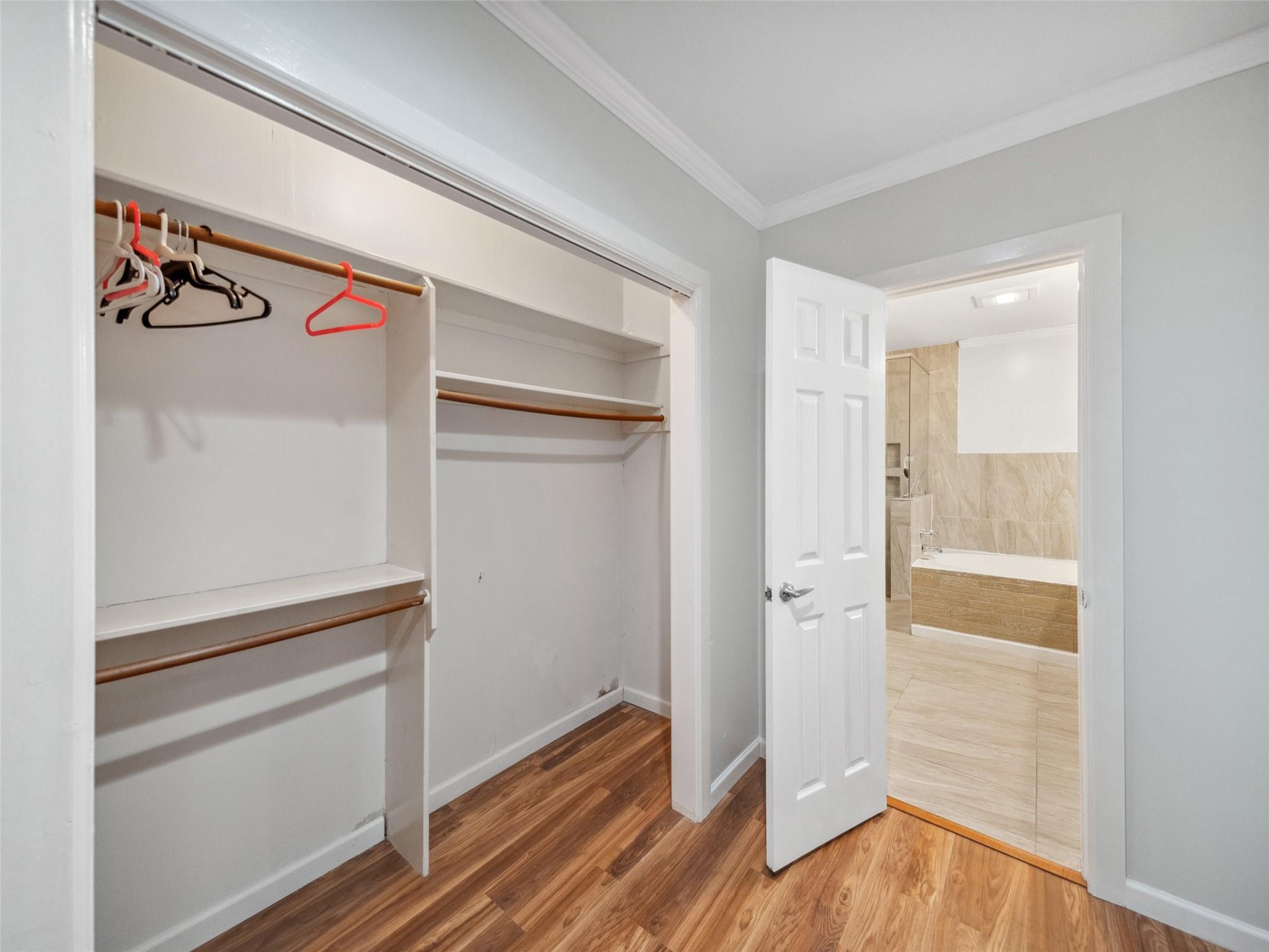 Walk-in closet with wooden rods and hangers, opening to a beige-tiled bathroom.