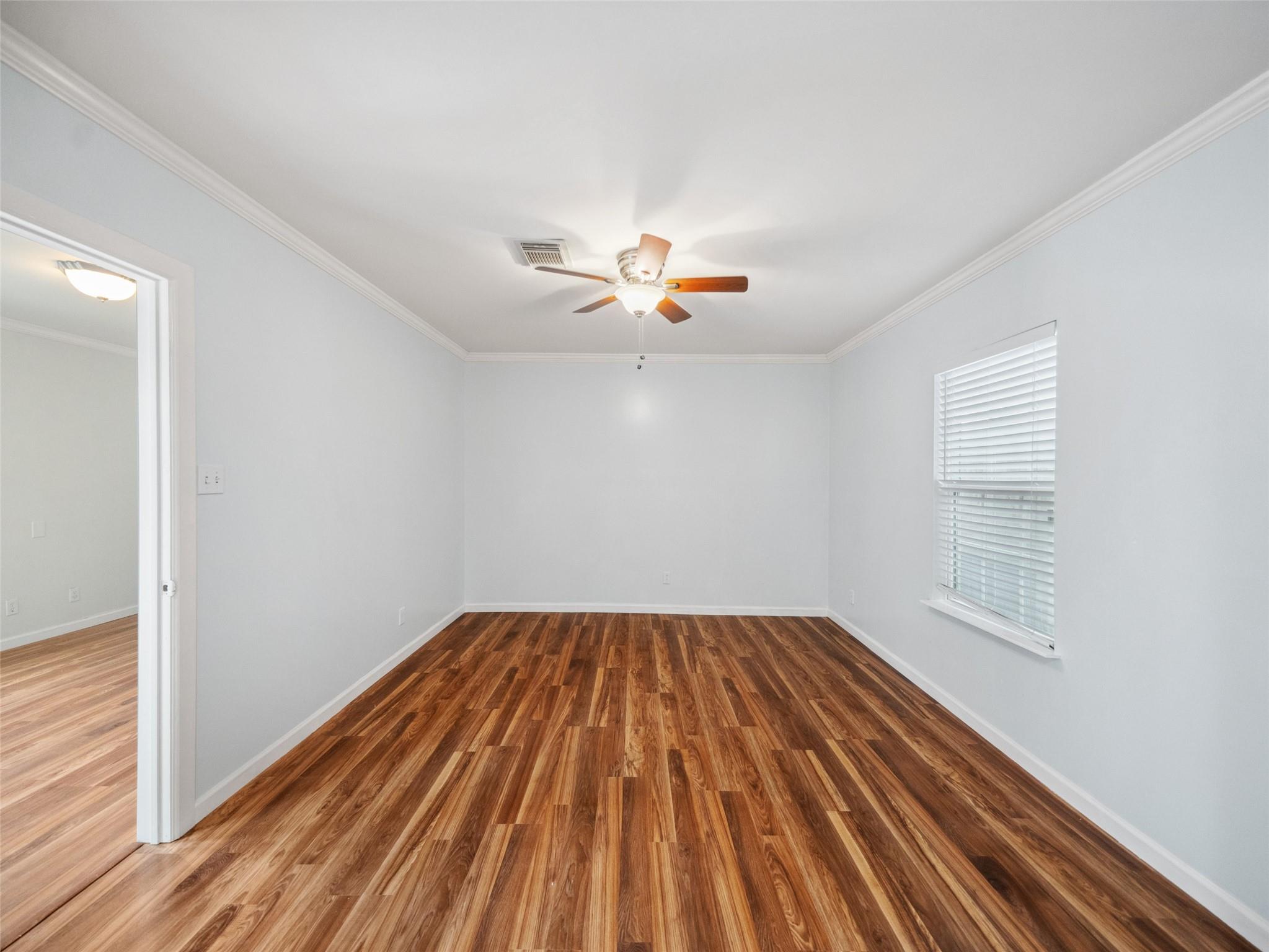 Empty room with wood-look flooring, a ceiling fan, and a window with blinds.