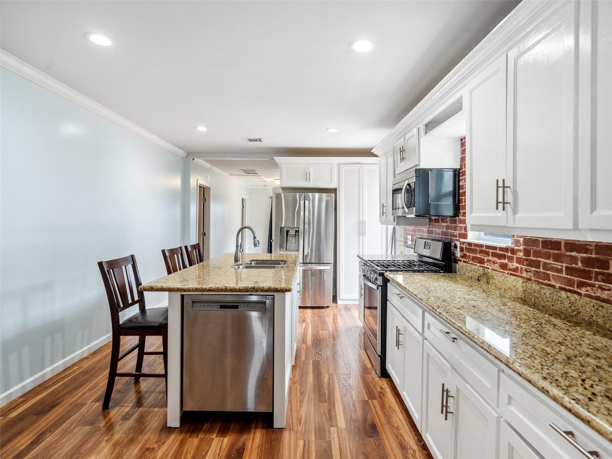 Kitchen with a granite island, stainless steel appliances, and a red brick backsplash.