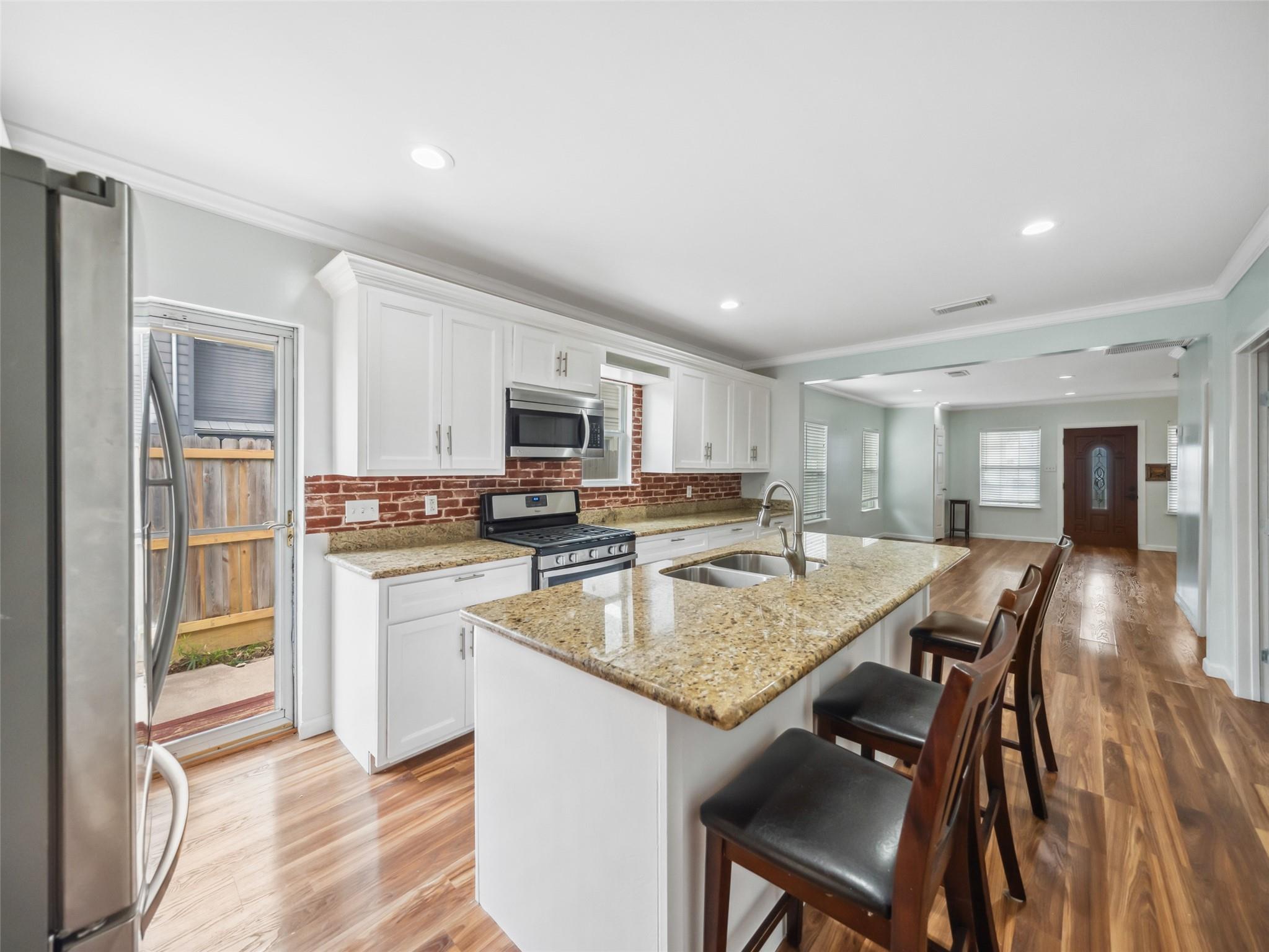 Kitchen with a granite island, brick backsplash, white cabinets, and stainless steel appliances.