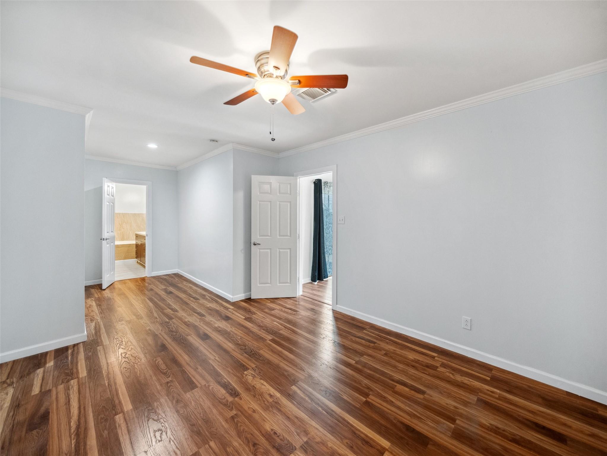 Empty bedroom with glossy hardwood floors, pale gray walls, and a ceiling fan with light.