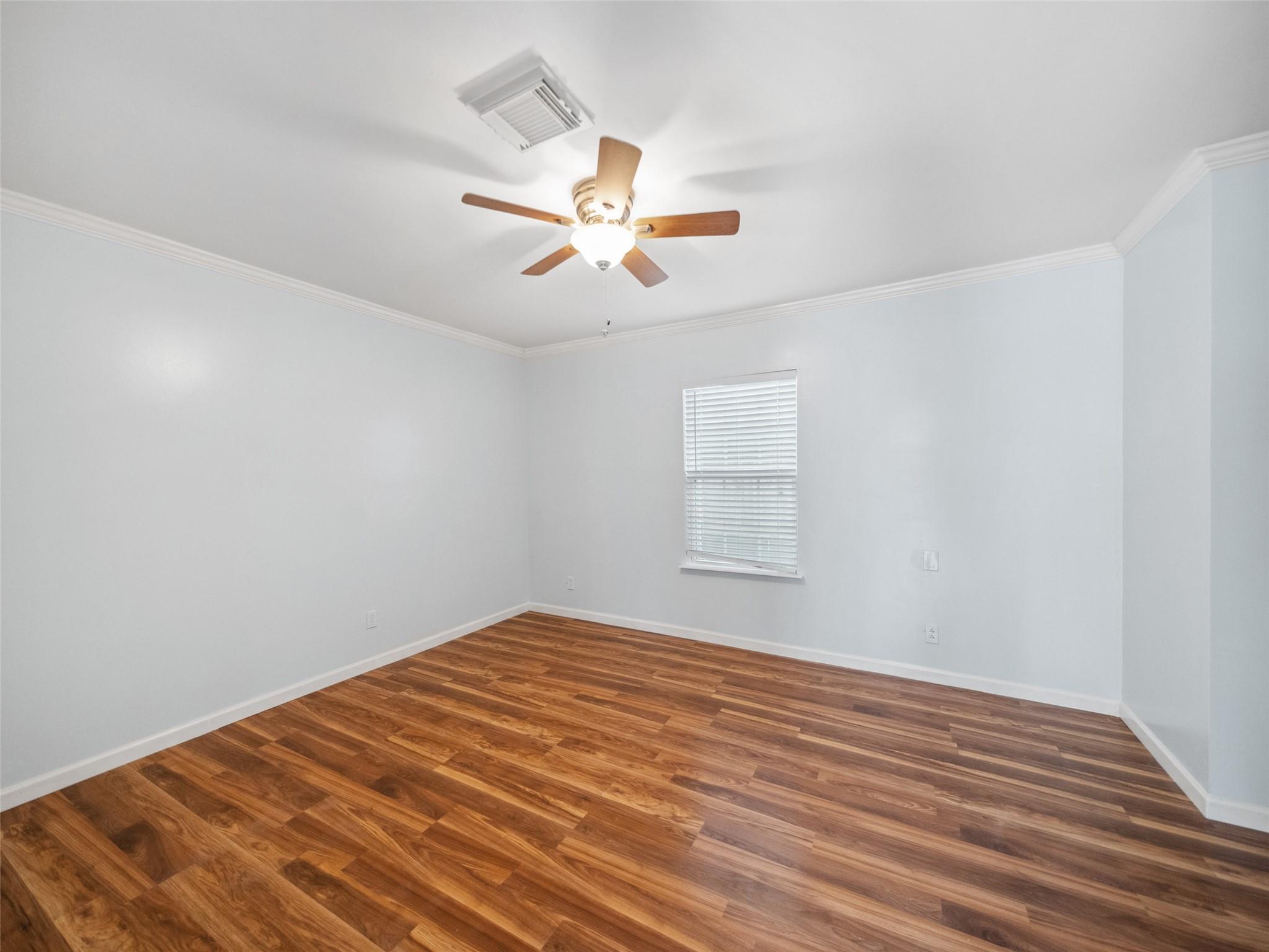 Empty room with warm-toned wood flooring, a ceiling fan, and a window with white blinds.