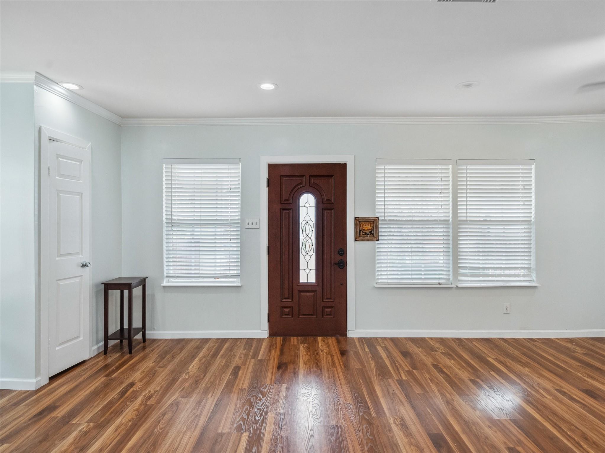 Entryway with a decorative glass front door, three shuttered windows, and warm hardwood floors.