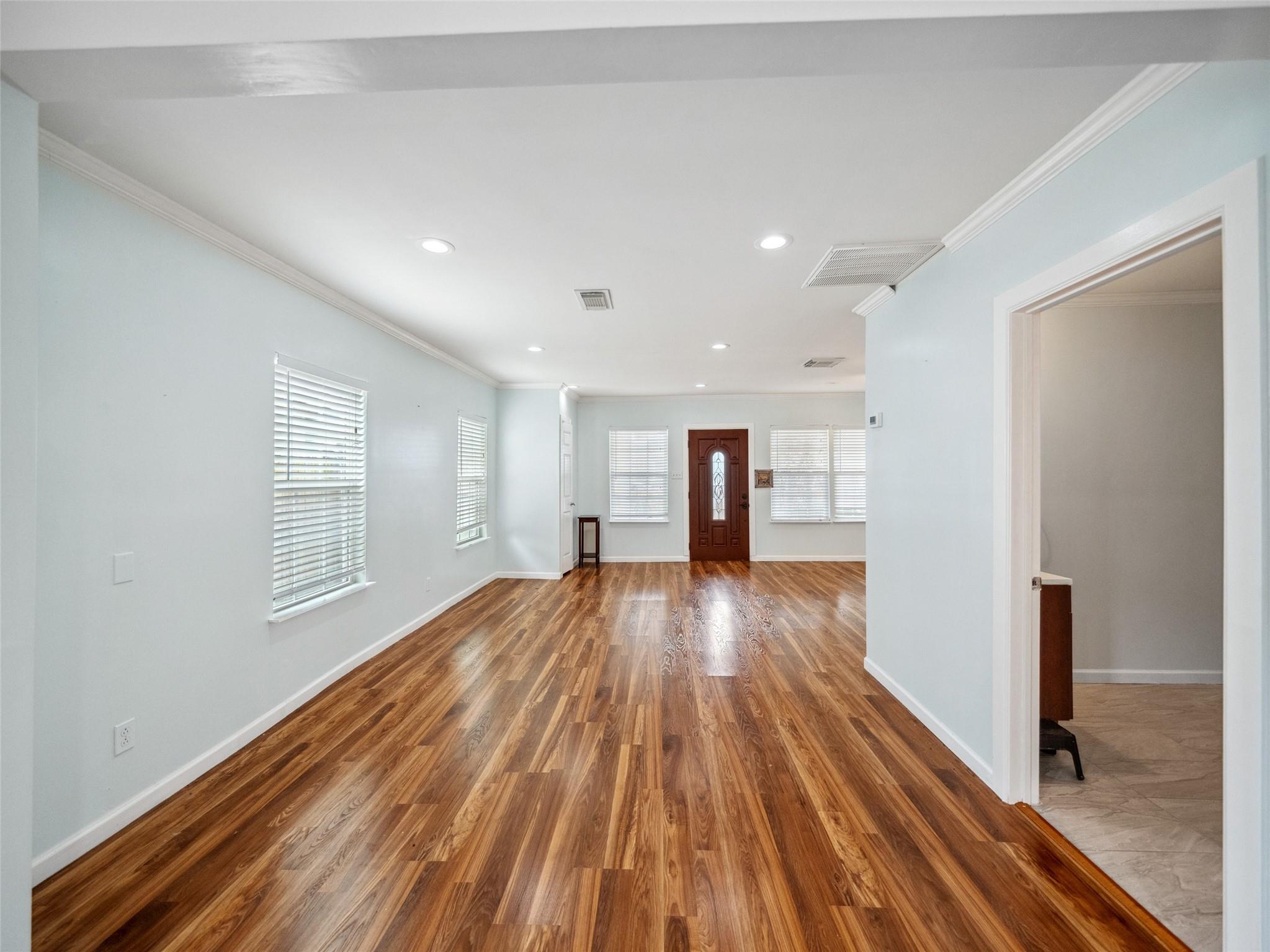 Empty living area with glossy wood floors, pale blue walls, and a decorative front door.