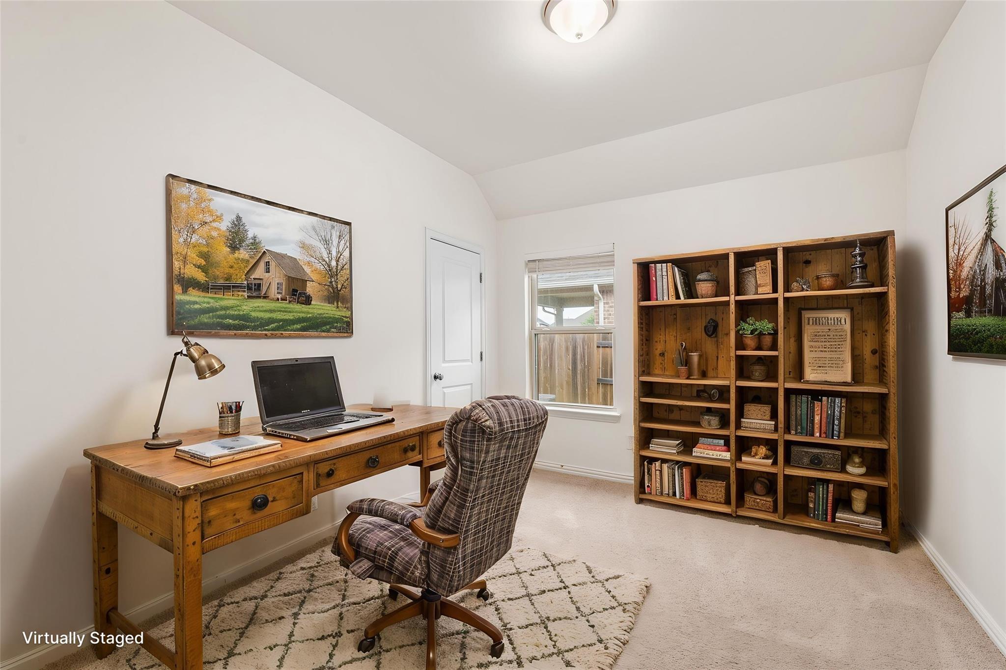Home office with a wooden desk, plaid chair, and large bookcase beneath a high angled ceiling.