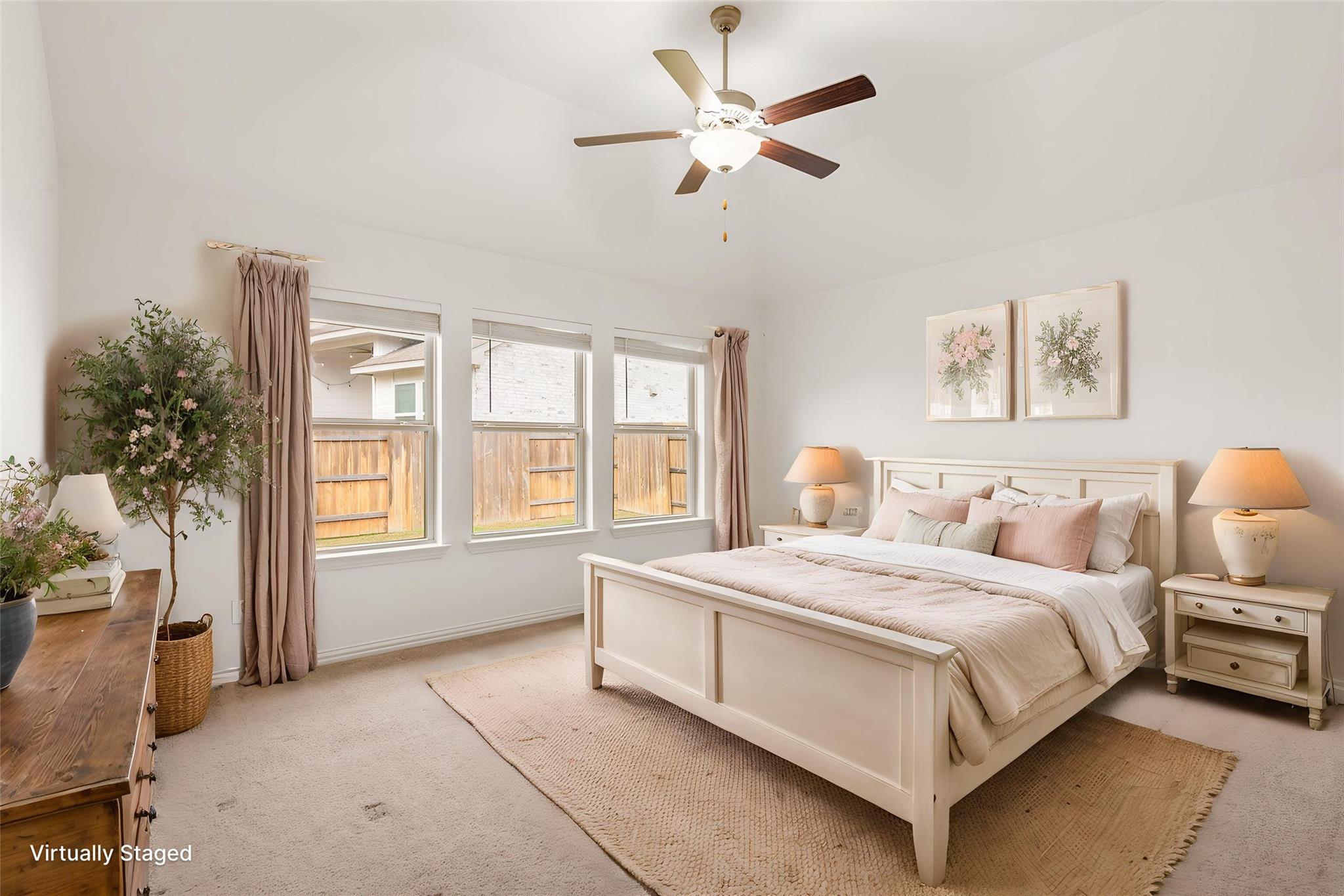 Staged bedroom with a white bed, three windows, and a ceiling fan.