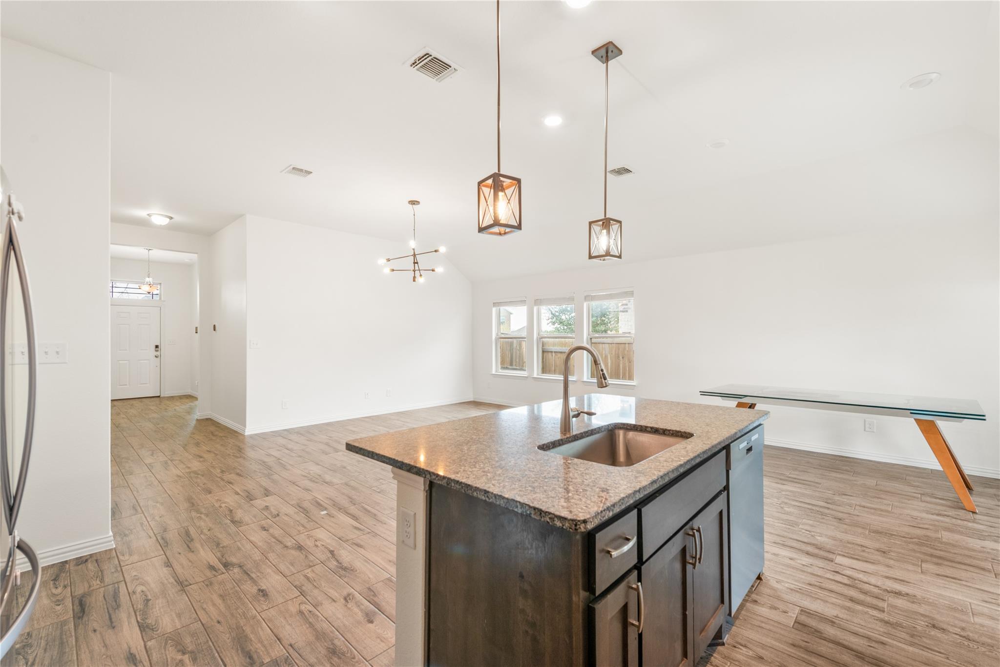 Open kitchen with a granite island, undermount sink, dark cabinets, and pendant lights.