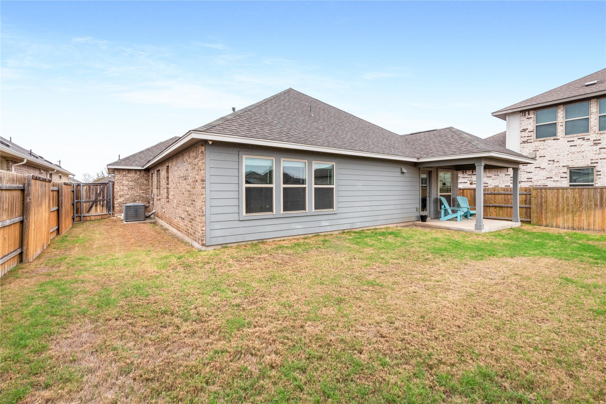 Home’s rear exterior with a covered patio, turquoise chairs, and a fenced backyard.