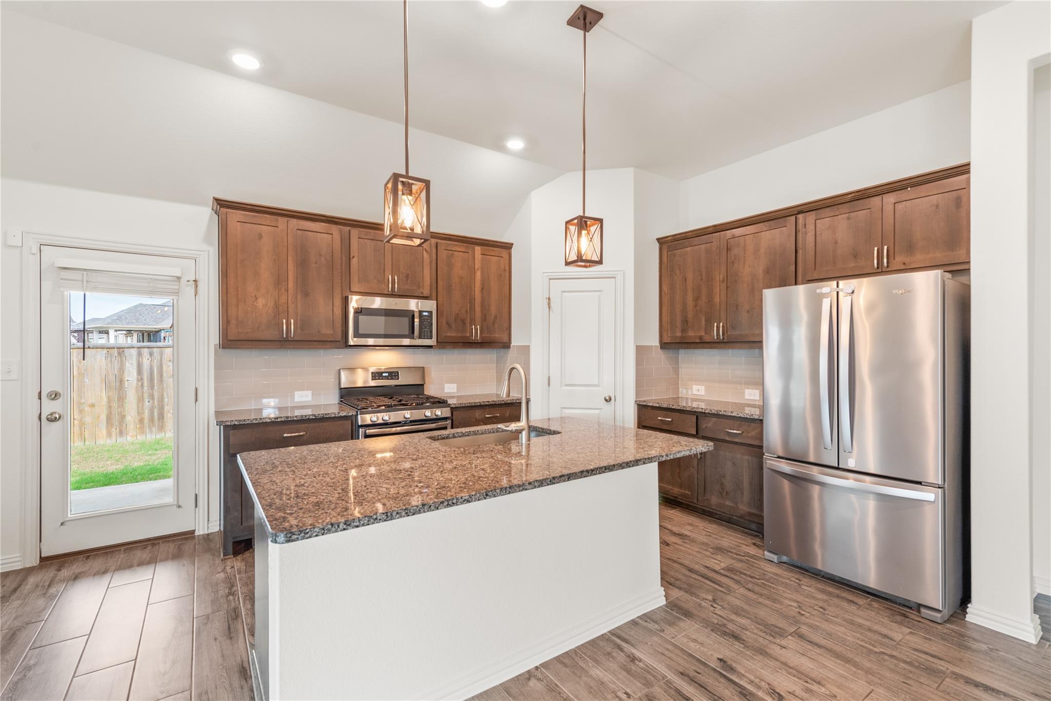 Kitchen with a granite island, dark wood cabinets, and stainless steel appliances.
