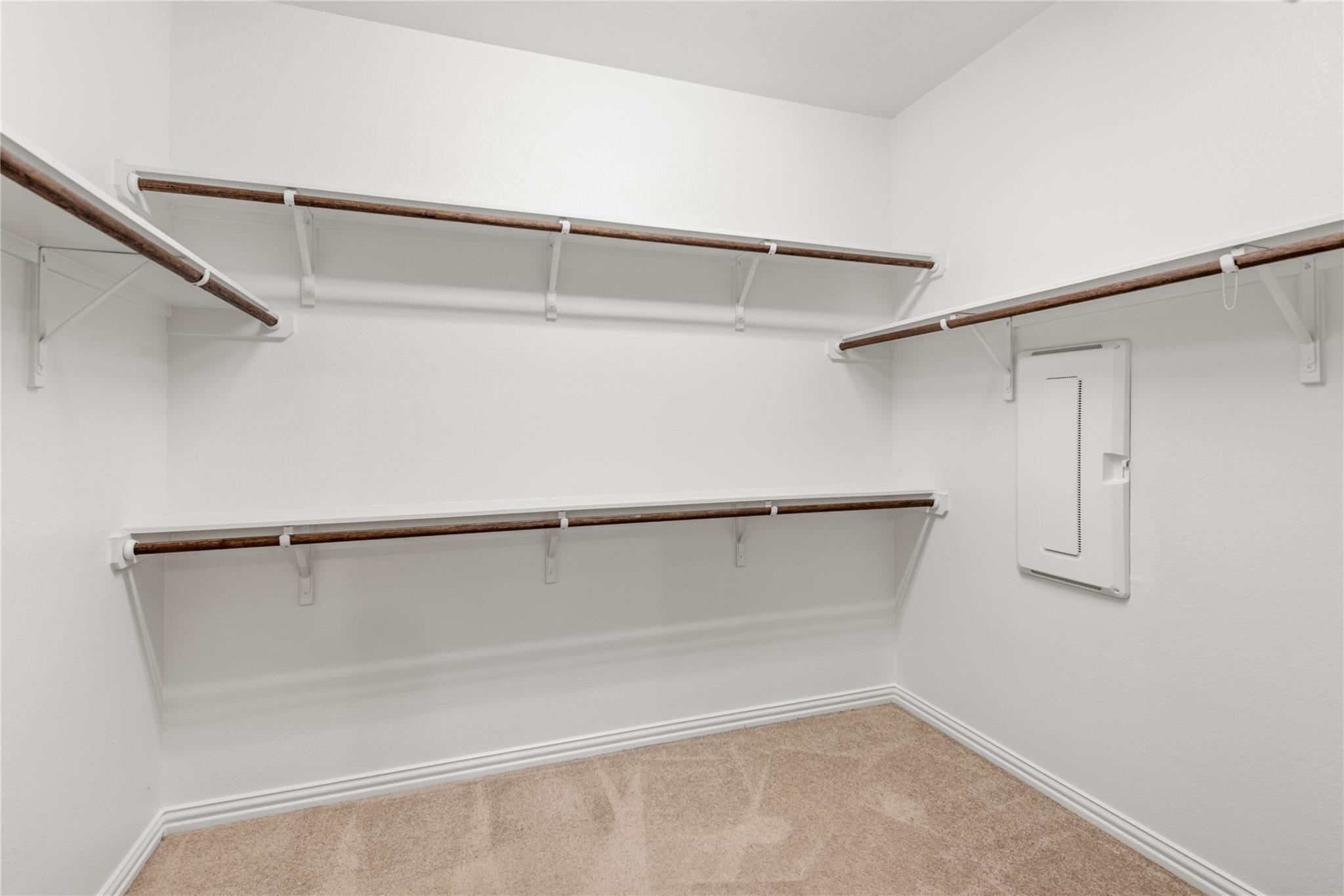 Walk-in closet with multiple wooden hanging rods, built-in shelves, and carpeted floor.