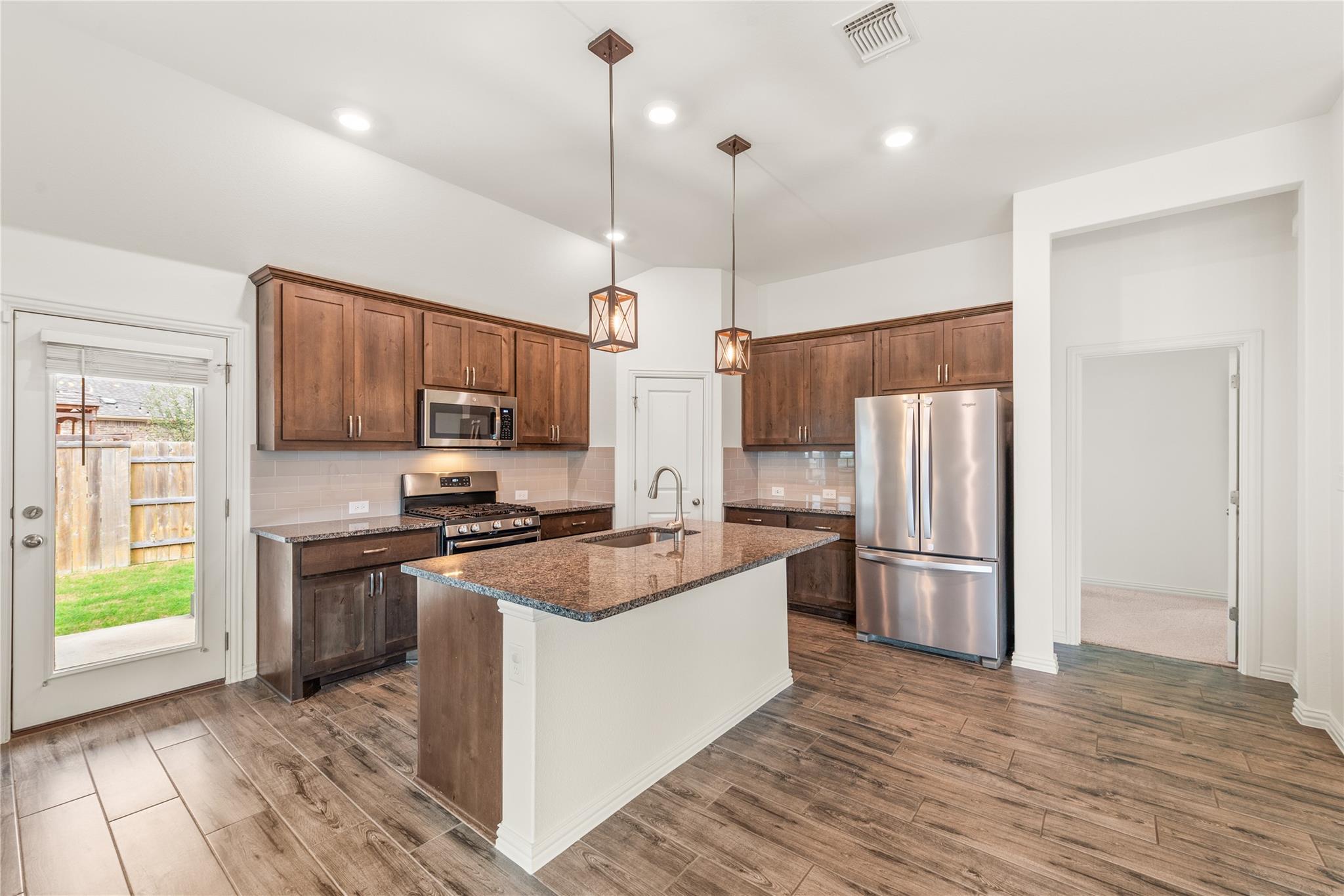 Kitchen with dark wood cabinets, granite island, stainless steel appliances, and a glass door to the yard.