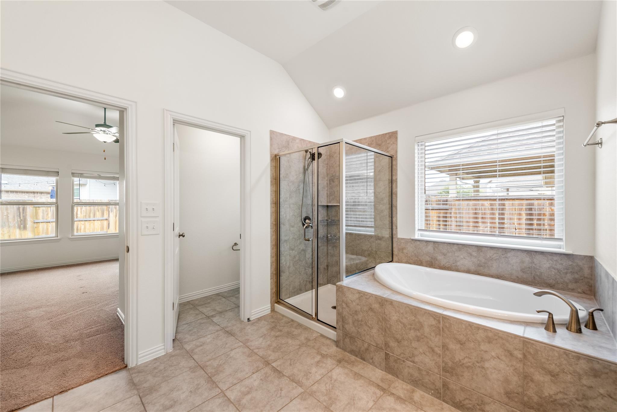 Tiled bathroom with a built-in soaking tub beside a glass-enclosed shower and large window.